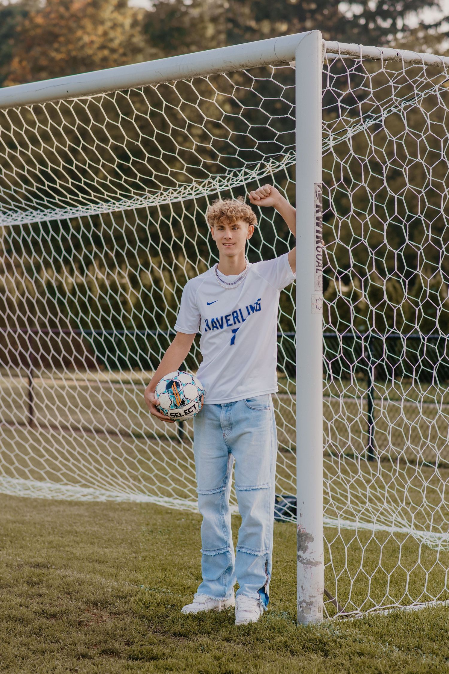 Casual soccer-themed photoshoot by goal post wearing denim and white t-shirt.