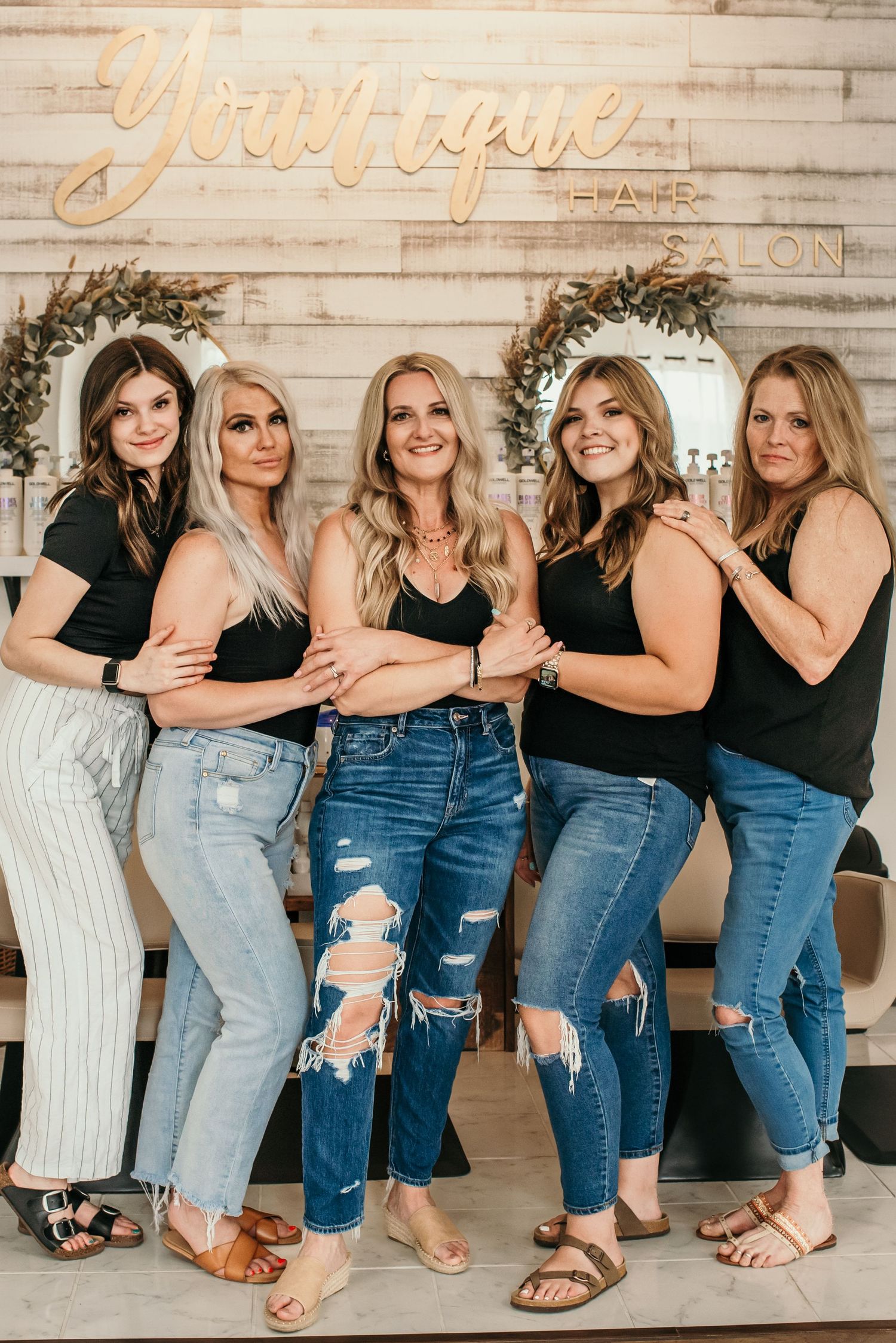Group photo of friends in matching outfits against rustic white wall with decorative signage.