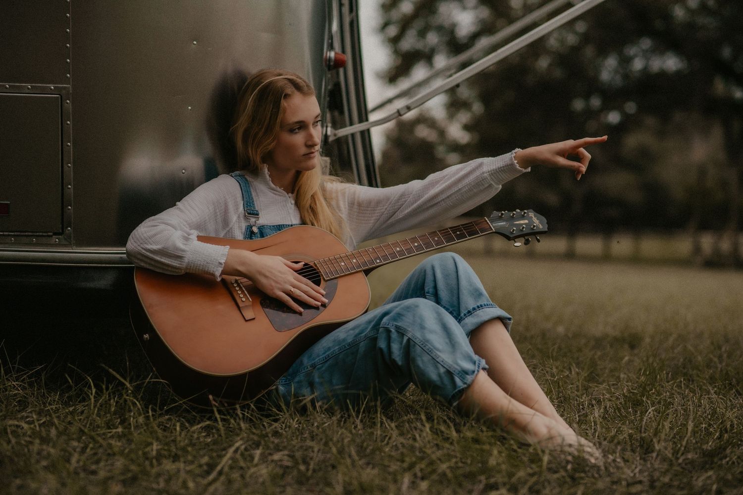 Person sitting in grass playing acoustic guitar in warm evening sunlight with moody atmospheric lighting.