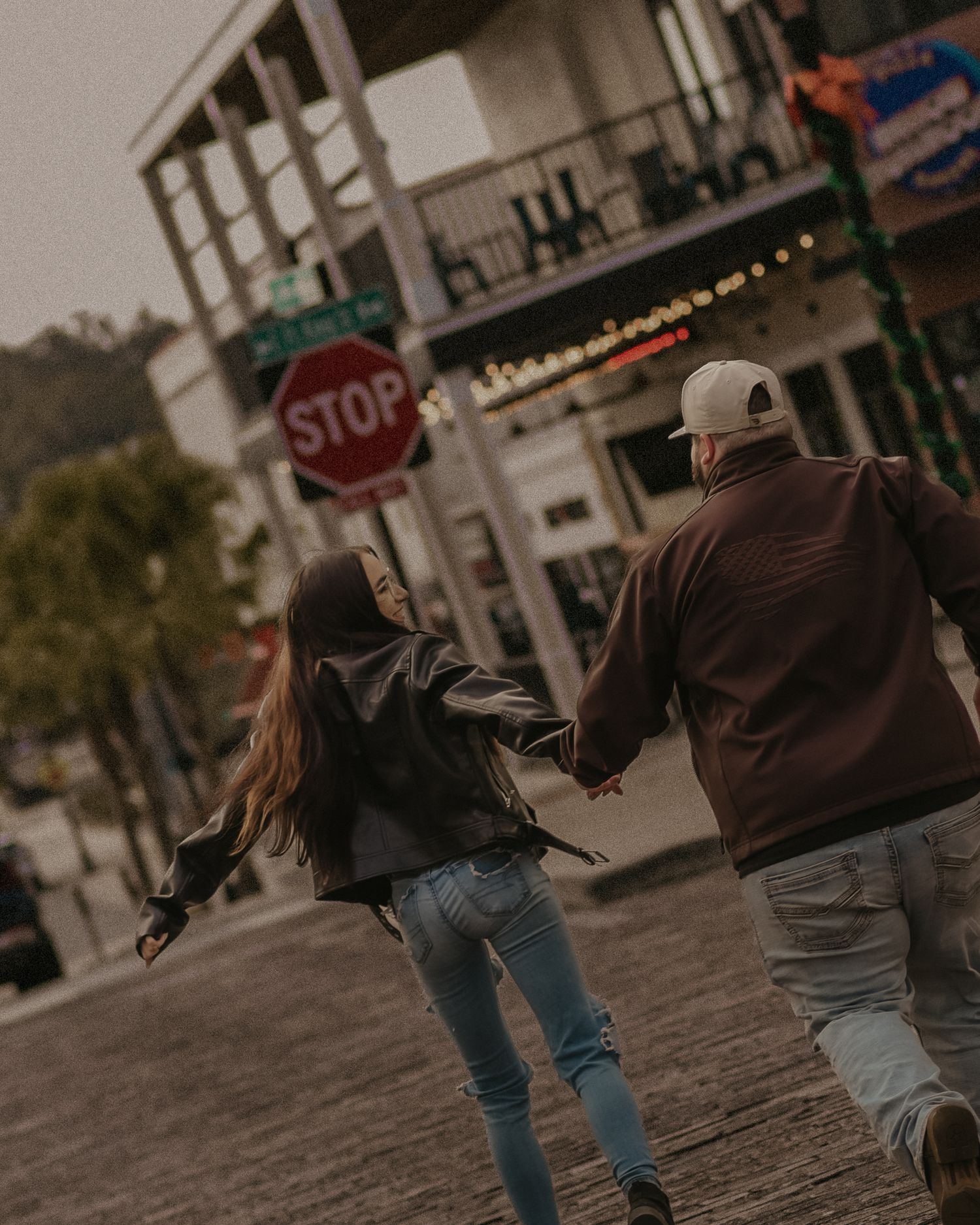 Three people walking away from camera on a cobblestone street with buildings visible in the background.