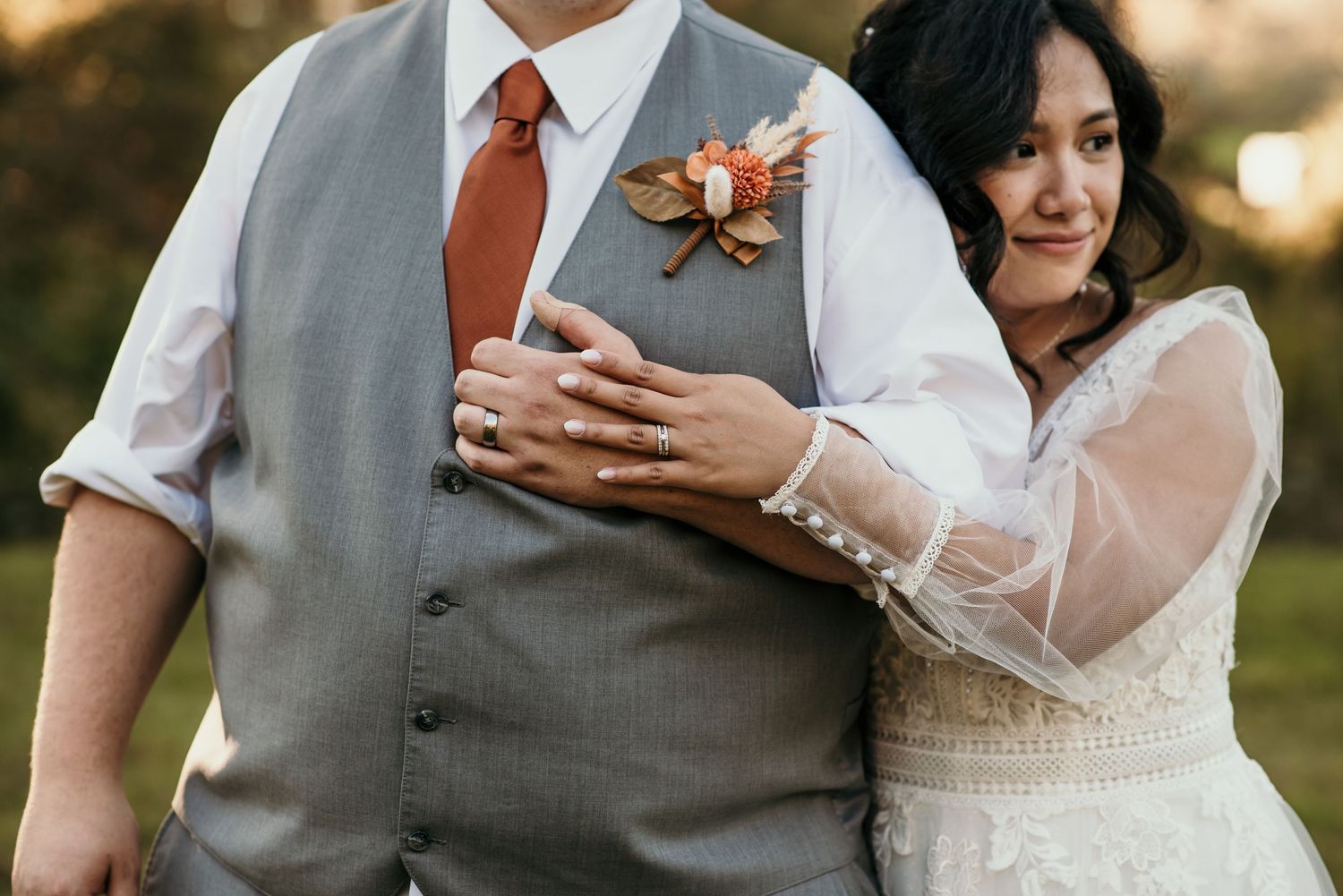 A close-up shot of a couple in wedding attire with the groom wearing a gray vest and orange tie.