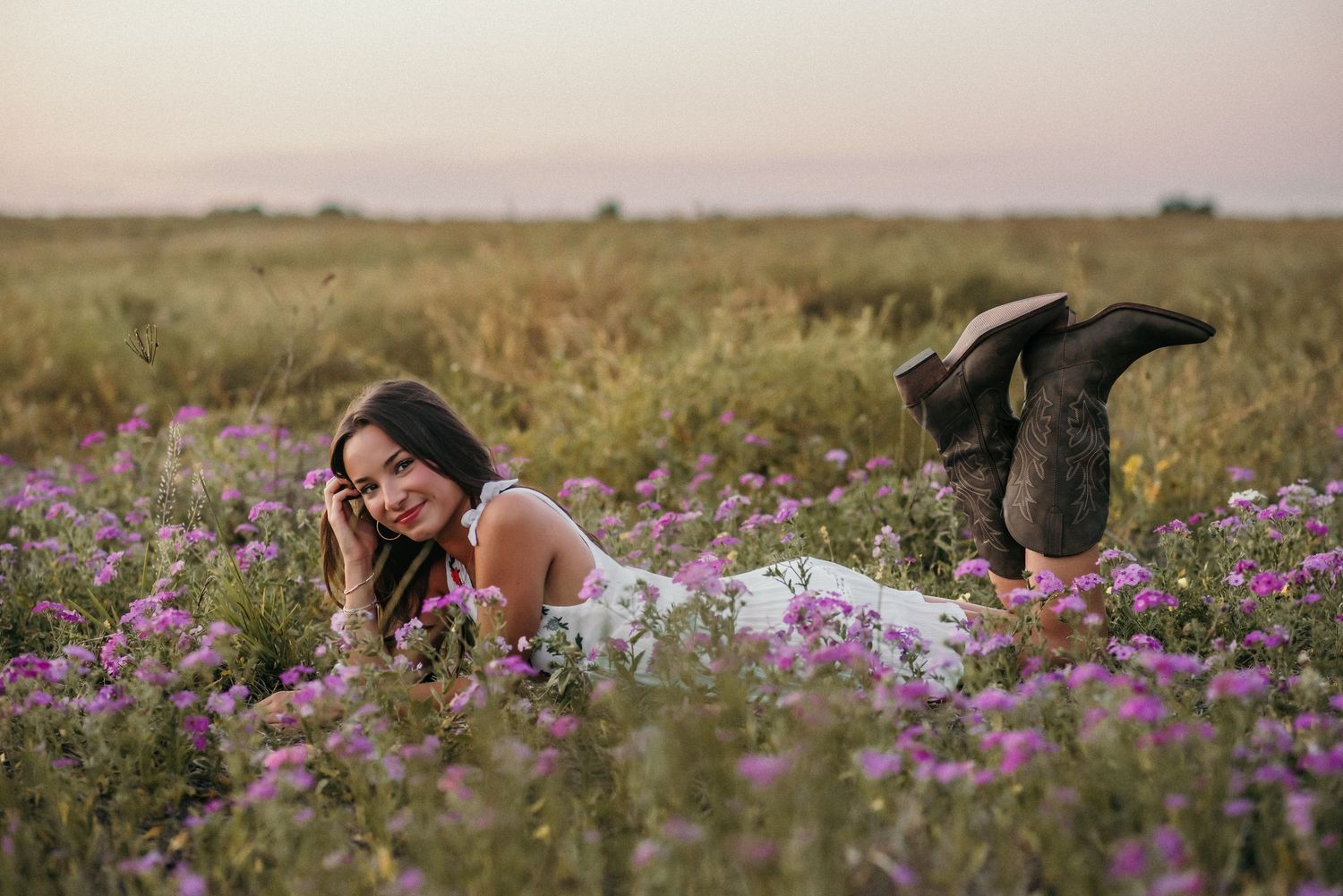A person relaxes in a blooming meadow wearing a white dress and dark boots.