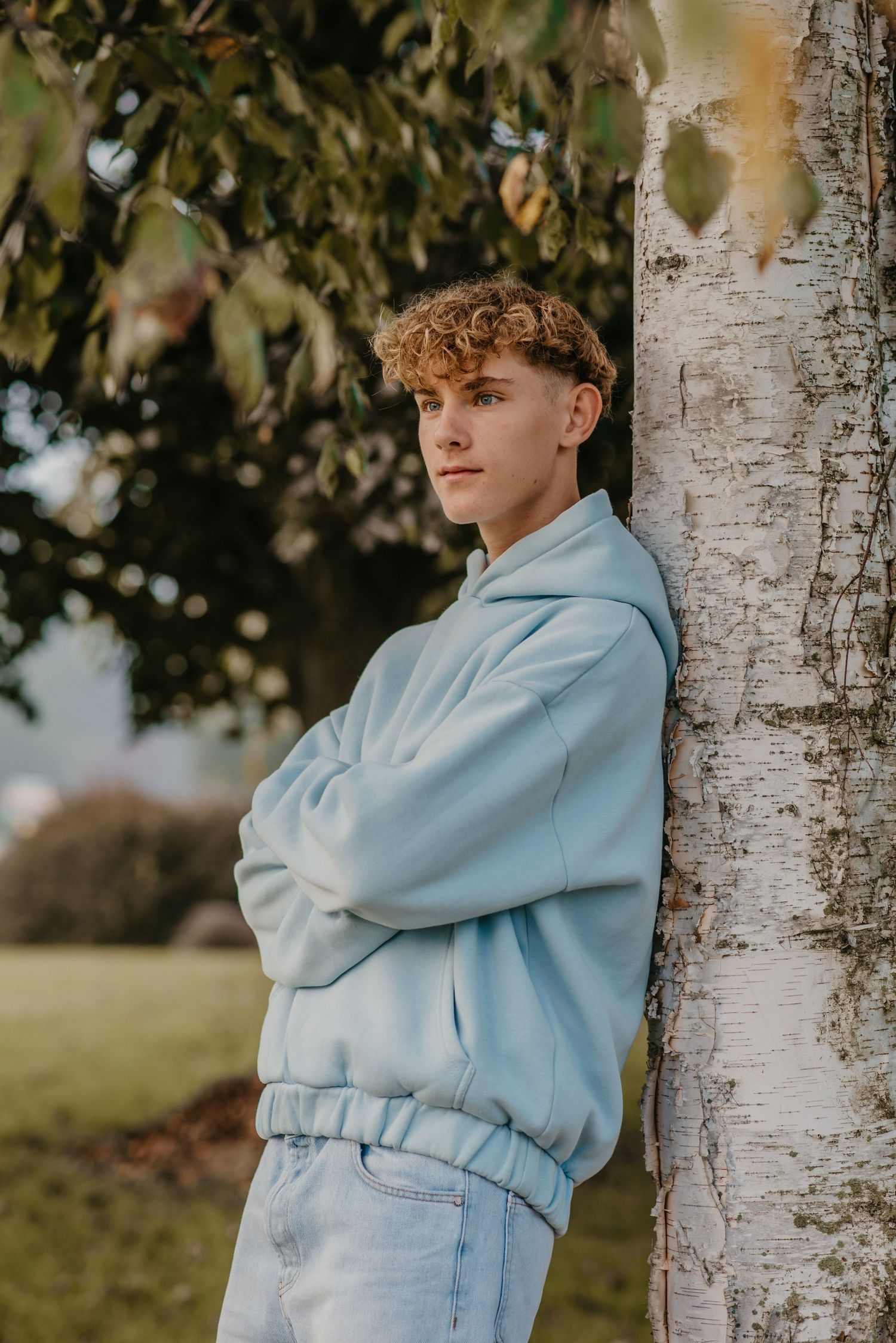 Casual outdoor portrait leaning against white birch tree in monochromatic blue outfit.