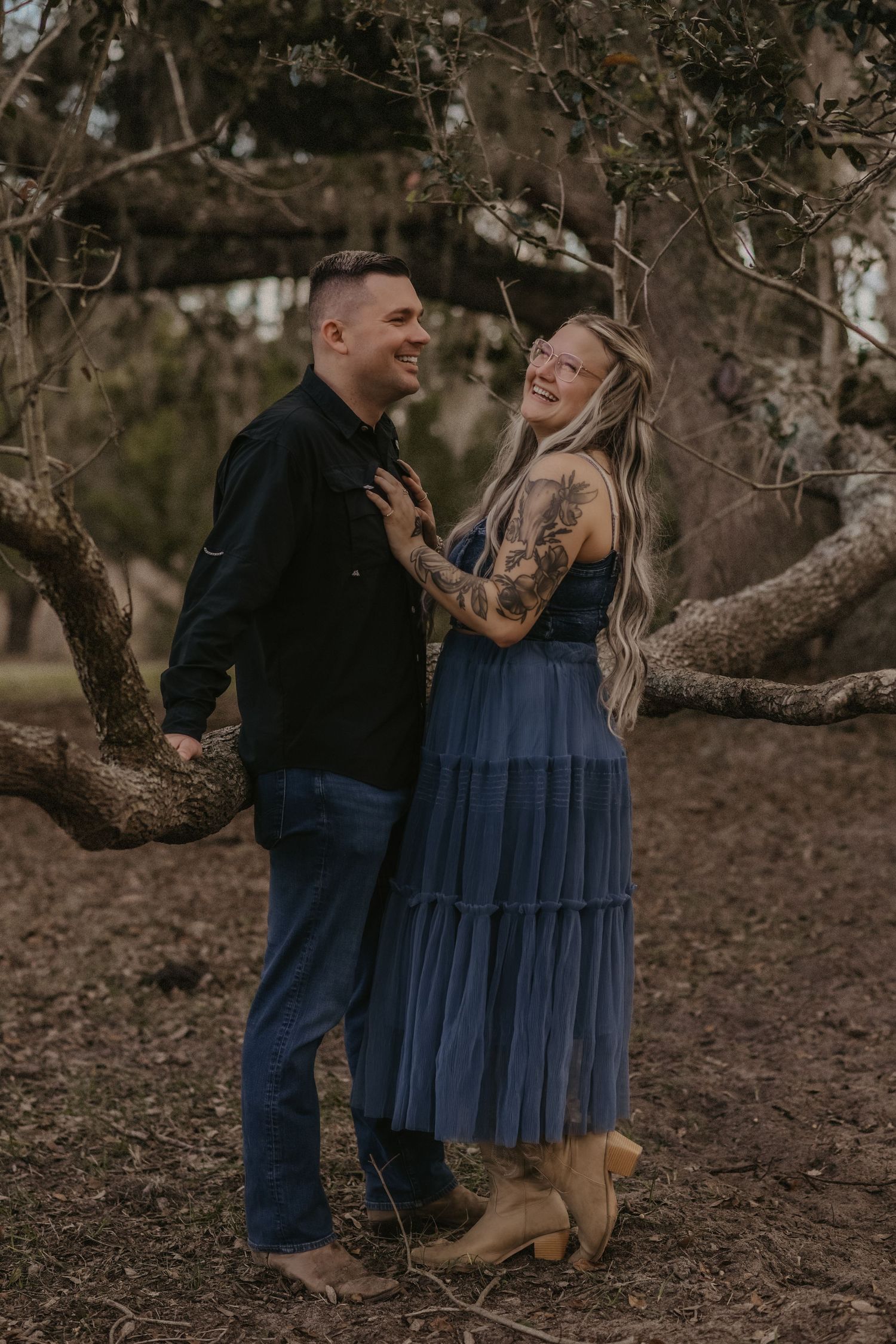 A couple shares romantic moments under twisted tree branches in a natural outdoor setting.