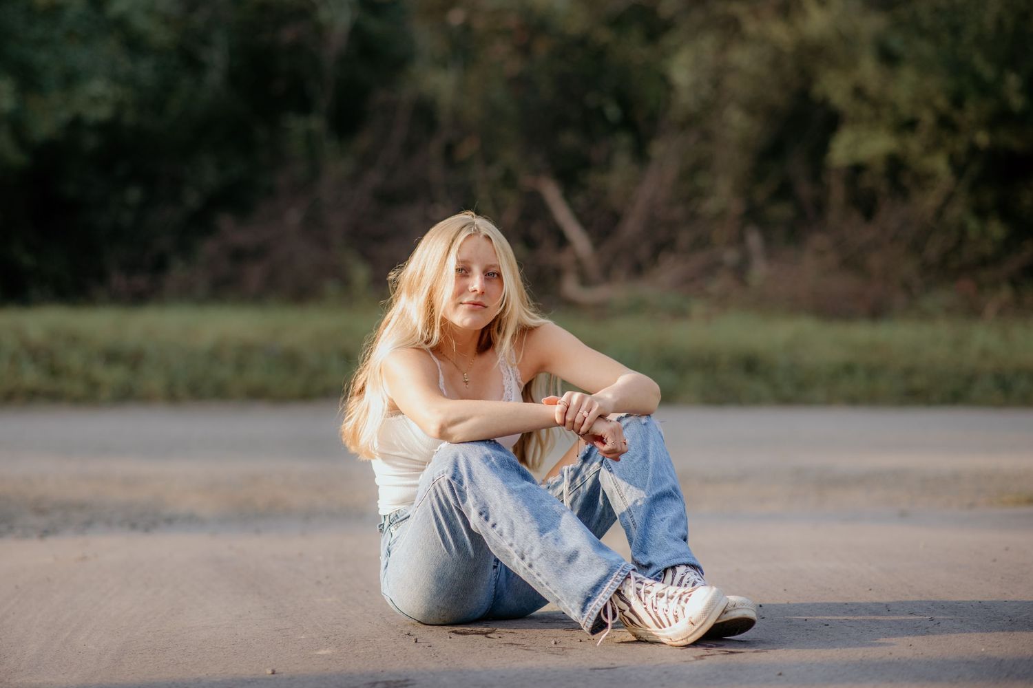 Candid sitting portrait on ground with distressed jeans and white top.