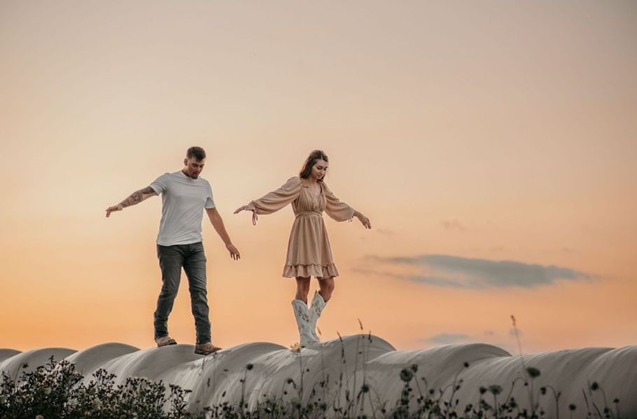 Playful couple with arms outstretched against sunset sky.