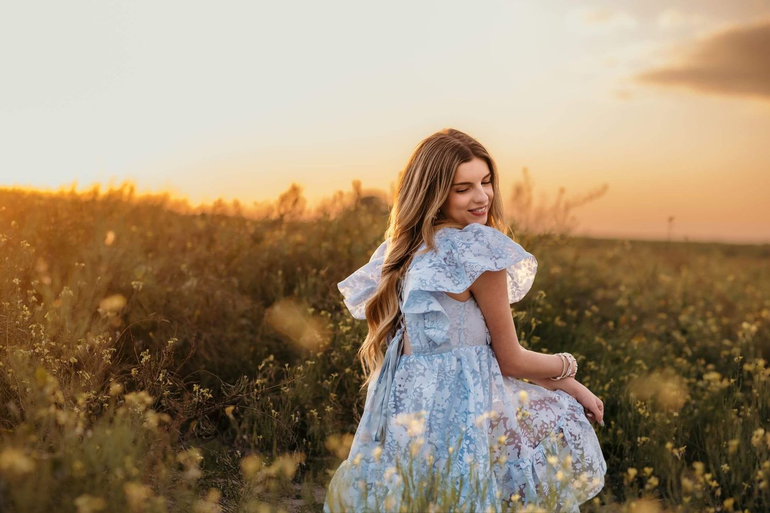 Dreamy sunset portrait of someone in a blue floral dress twirling in a golden field.