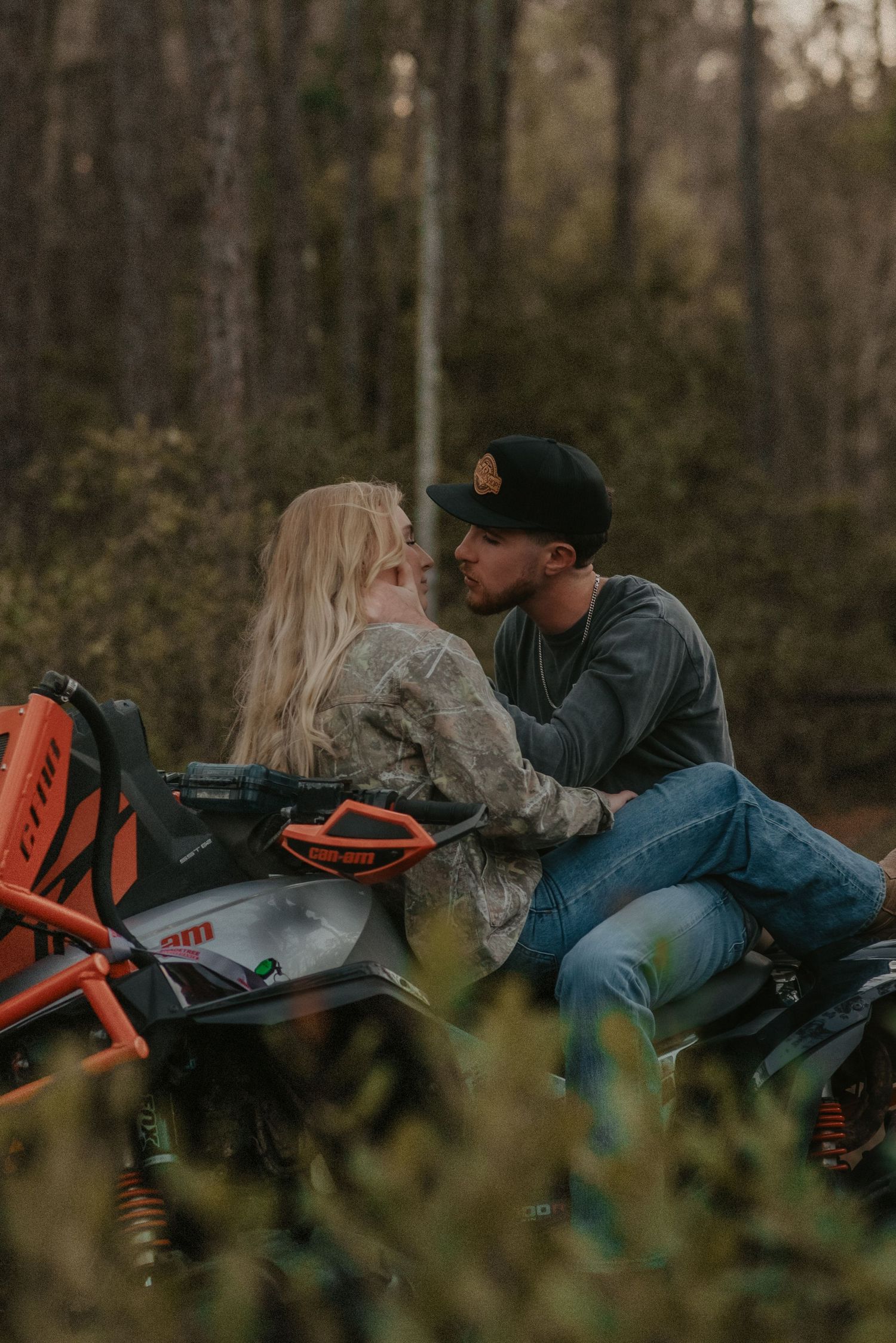 A couple relaxes together in tall grass during an intimate outdoor photo session in a moody forest setting.