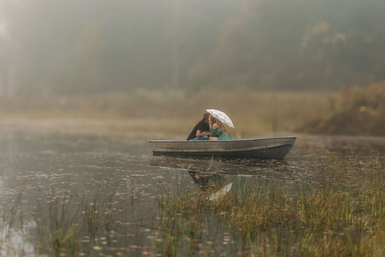 Silhouetted boat glides across misty lake at dawn with reflective water and atmospheric morning light.