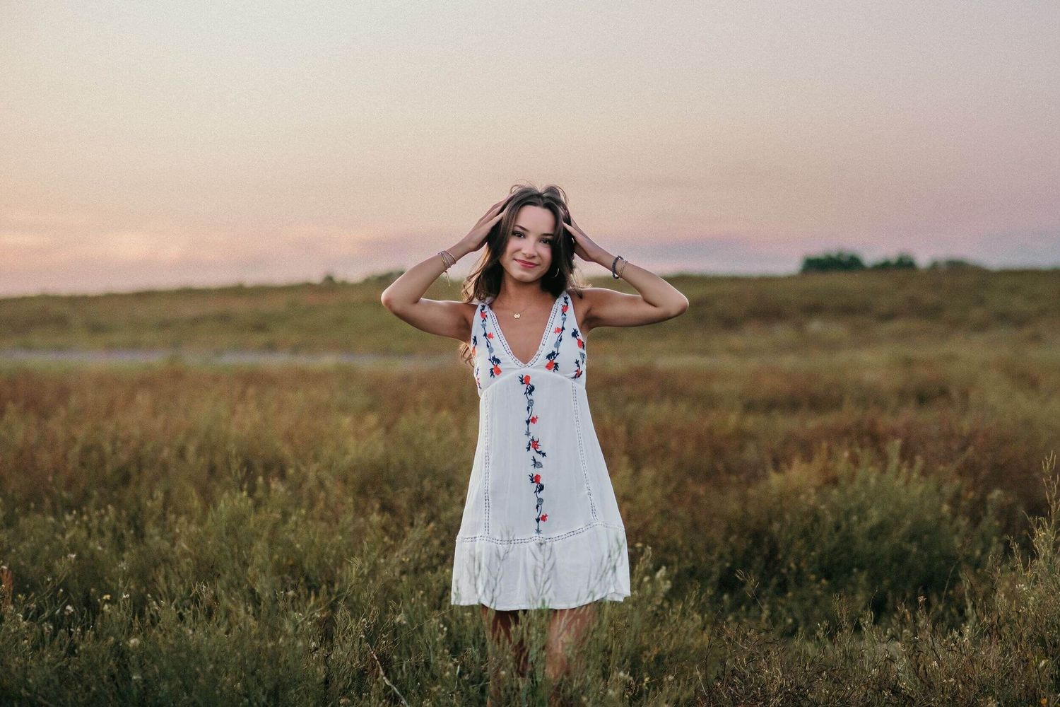 Someone in embroidered white dress poses in wildflower field during golden hour.