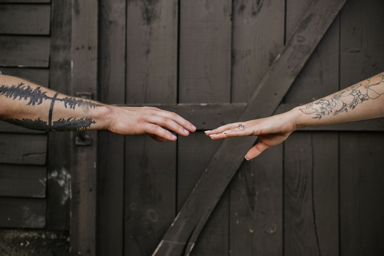 Two tattooed hands reaching towards each other against a dark wooden background.
