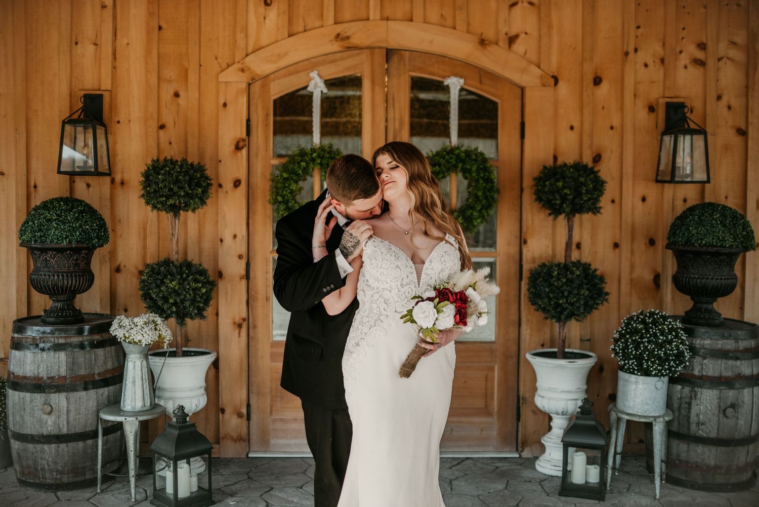 A couple shares a romantic moment in front of a rustic wooden barn door with decorative lanterns.