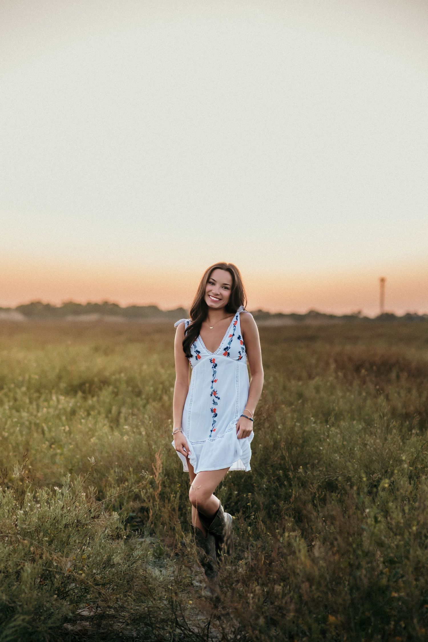 A white summer dress stands out in a golden field at sunset with boots.
