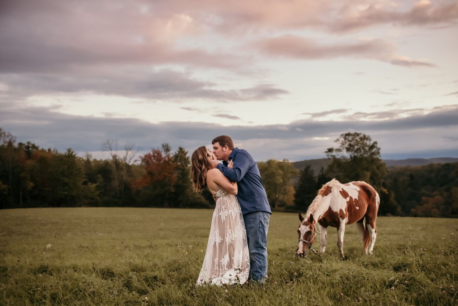 Romantic sunset photoshoot in a scenic field with mountains in the background.