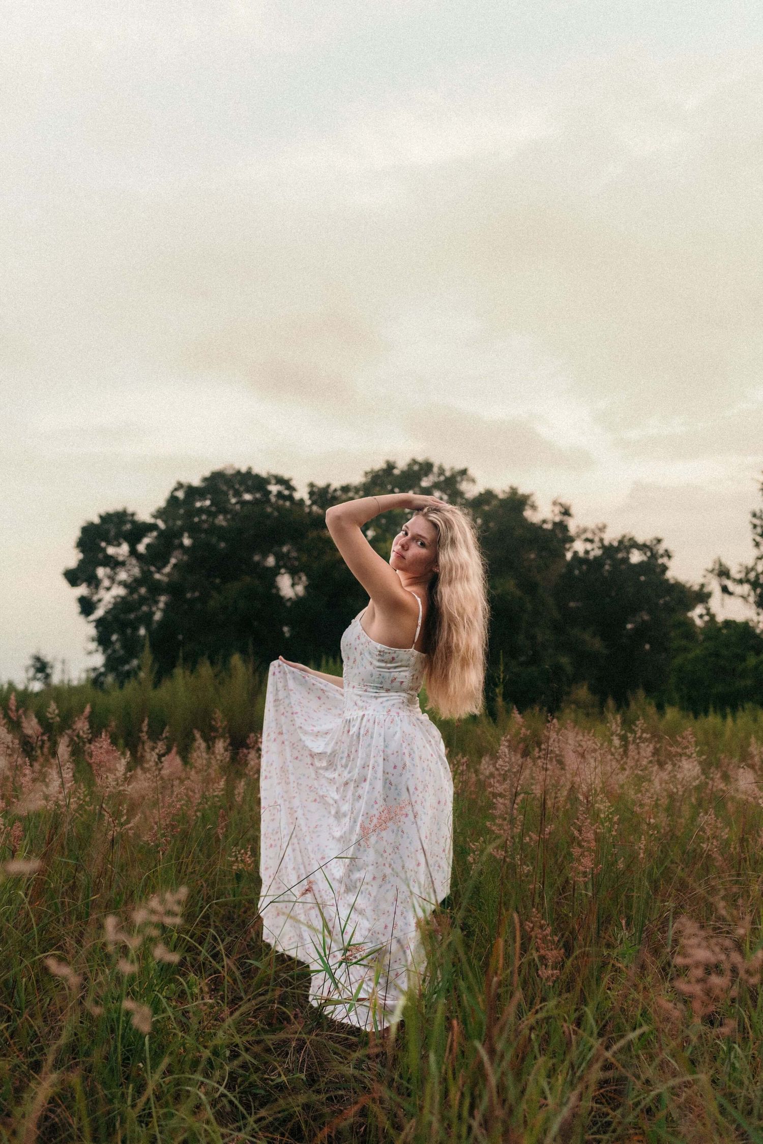 White lace dress flowing in a rustic field during golden hour with soft clouds overhead.