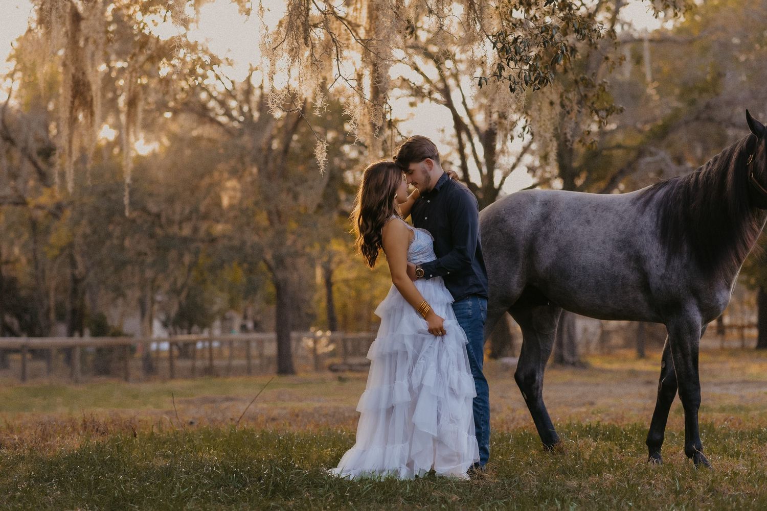 A romantic wedding photoshoot in a rustic outdoor setting with a black horse at sunset.
