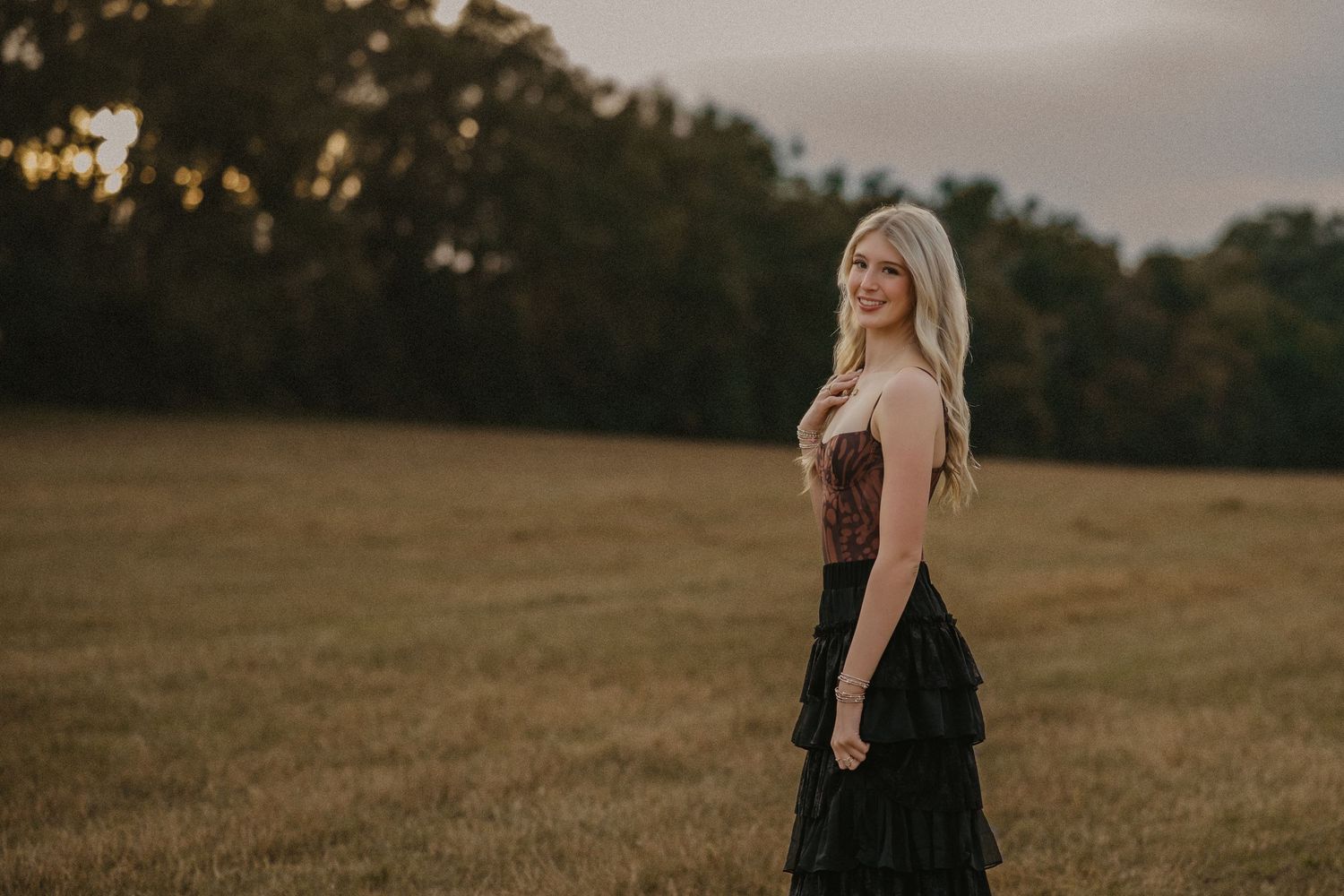 A woman in a black dress walks through a golden field at sunset creating a dreamy silhouette.