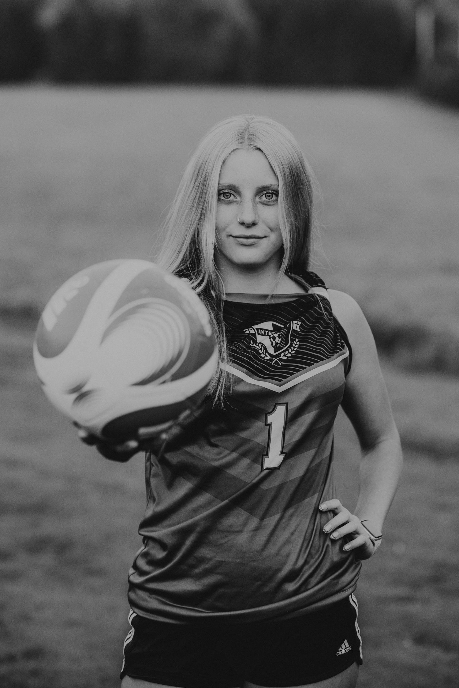 An athlete in a sports jersey poses with a volleyball against a blurred background.