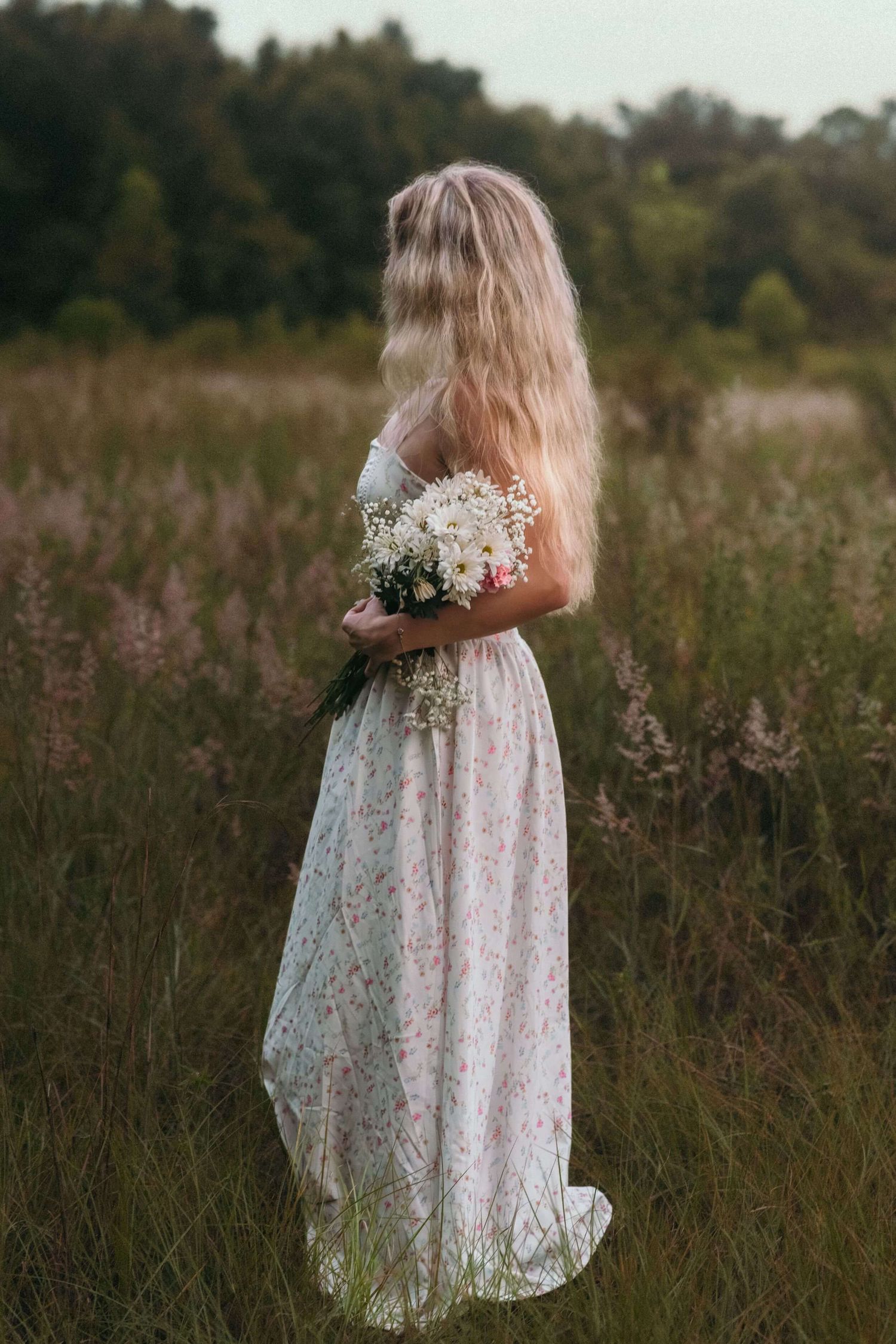 Delicate lace dress and wildflower bouquet in a summer meadow at sunset.