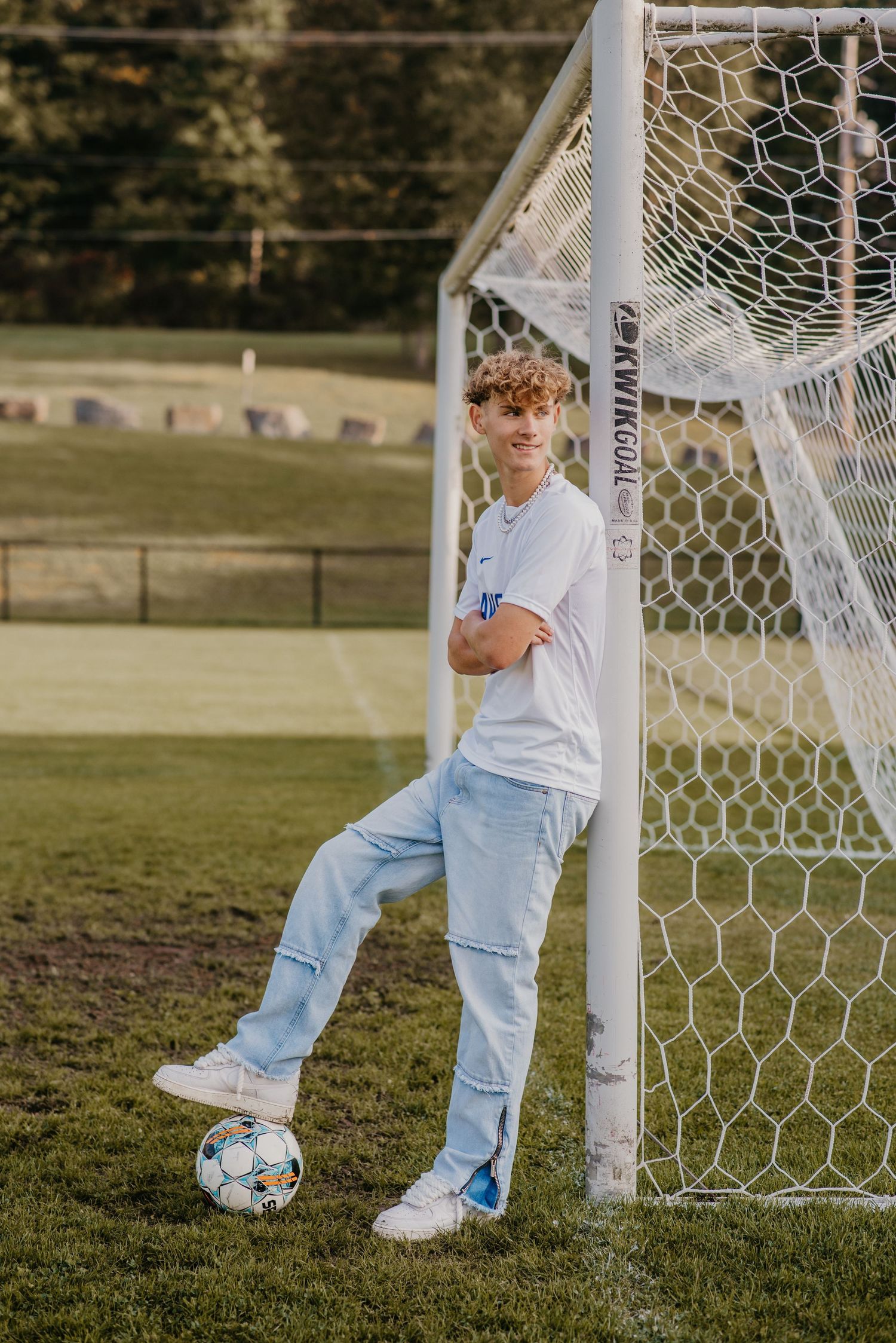 Athletic pose with soccer ball against goal post on grass field at sunset.