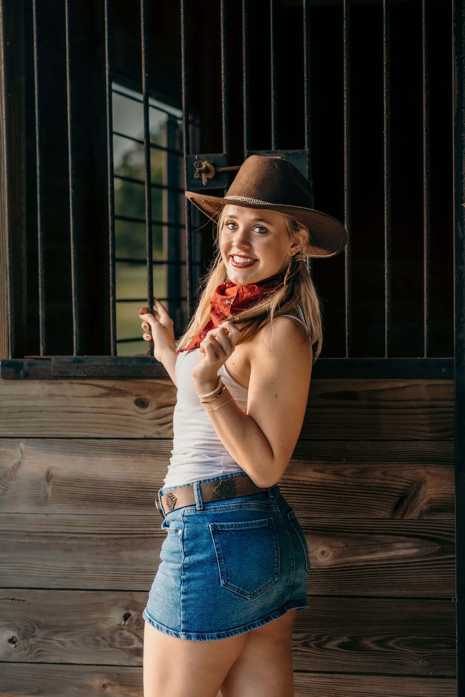 Cowgirl style portrait with brown hat and red bandana against rustic wooden backdrop.