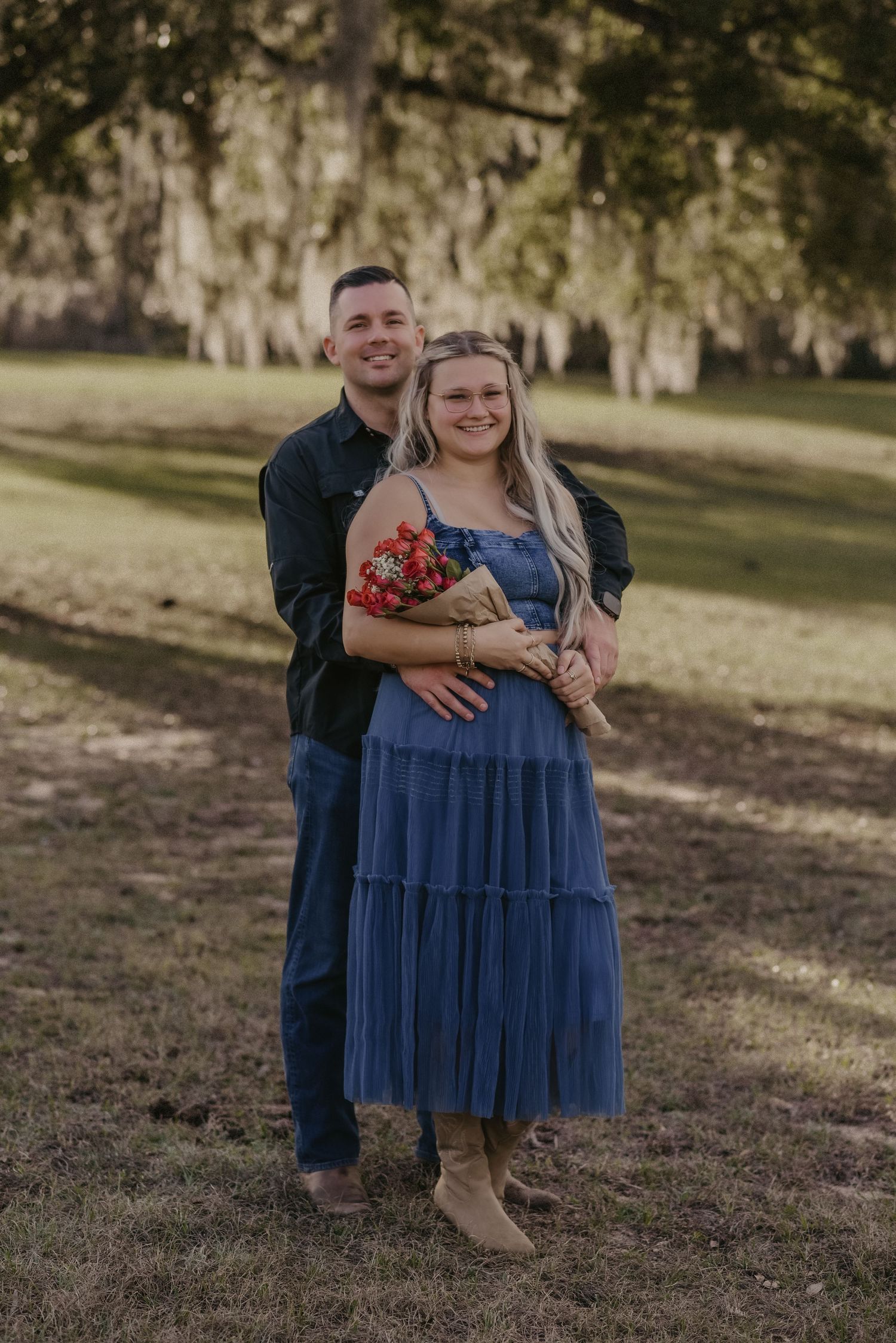 A couple shares a romantic moment outdoors on grassy terrain in a casual engagement photo session.