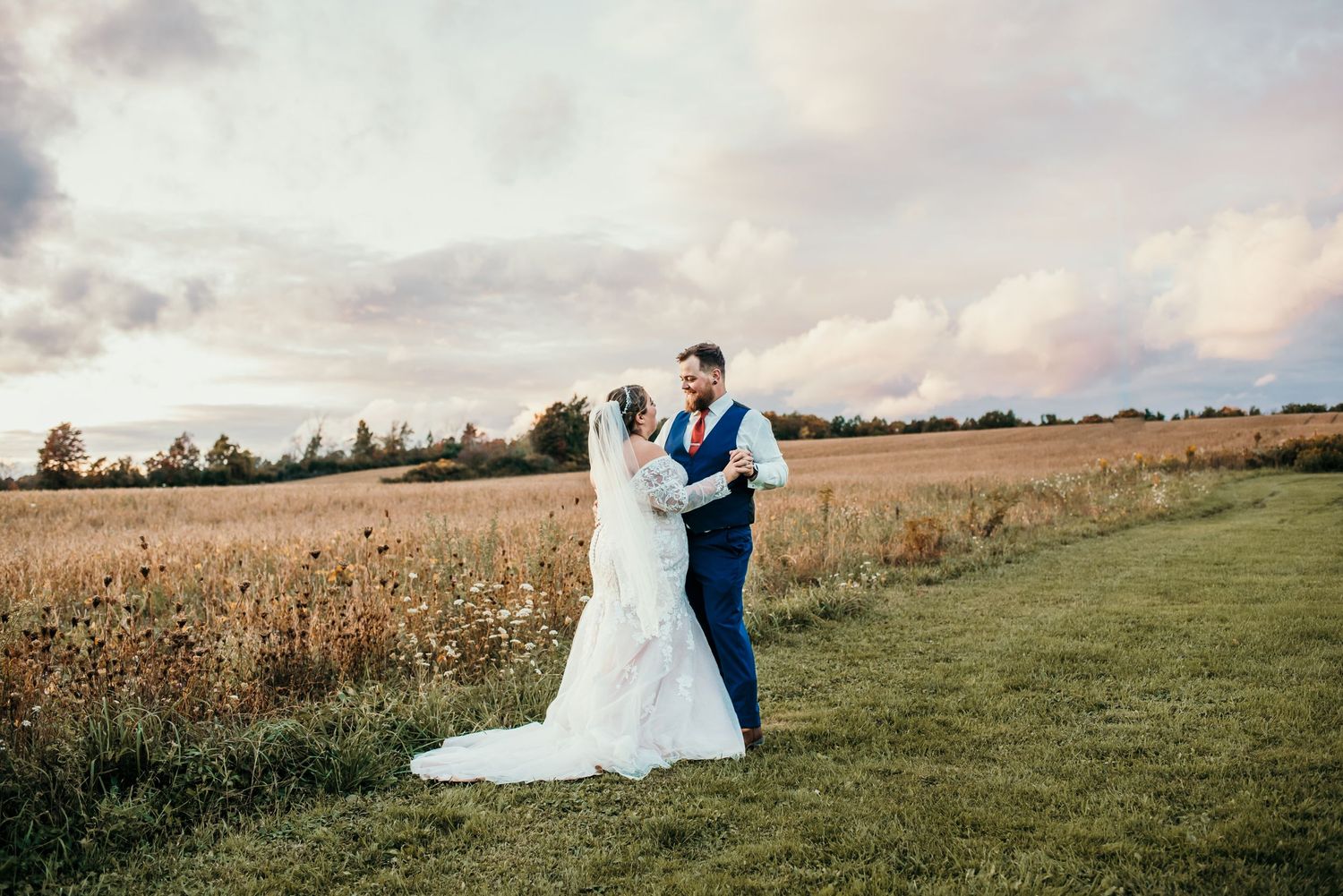 Newlyweds posing together in an open field during golden hour.