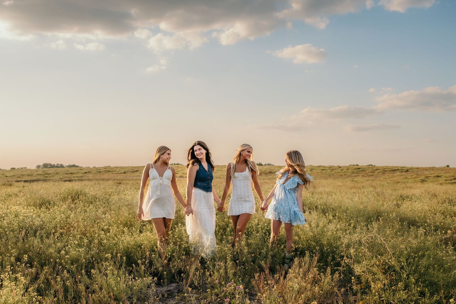 A group stands together in flowing dresses against a sunset prairie landscape.