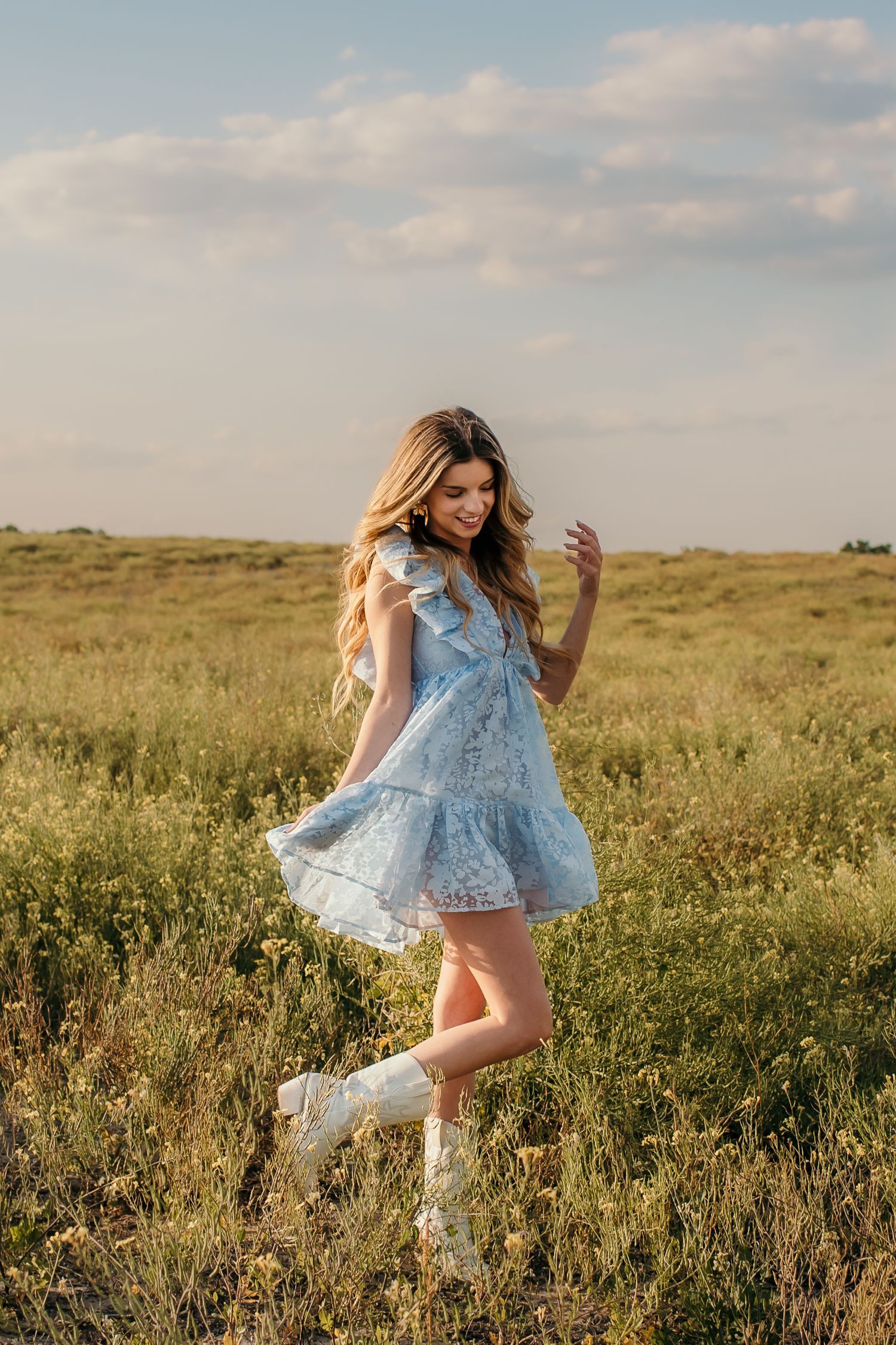 Woman in light blue dress twirling through wildflower field at sunset.
