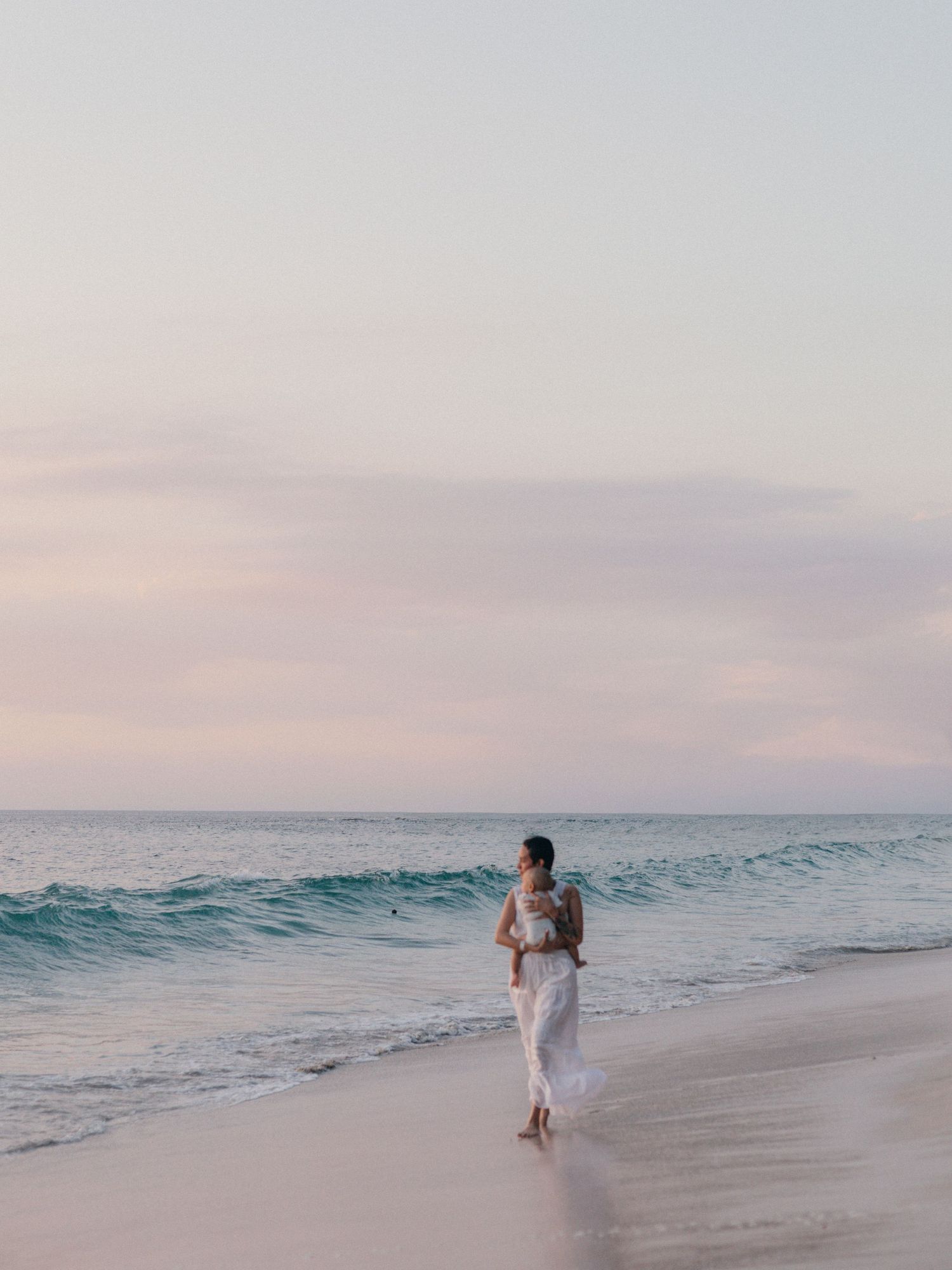 Photo by Bendito Recuerdo in Costa Rica, blurry photo of mom holding baby walking by the coast of a Pacific Ocean beach in Costa Rica