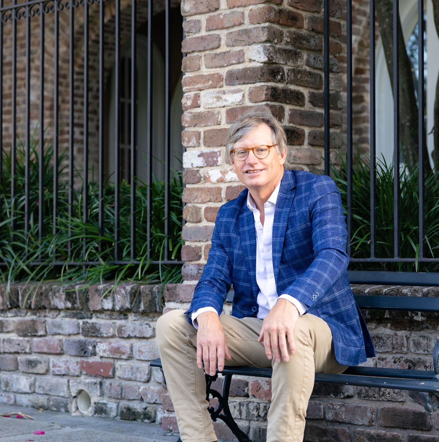 Man in blue plaid blazer sitting on brick steps outside a building, smiling casually in natural light.
