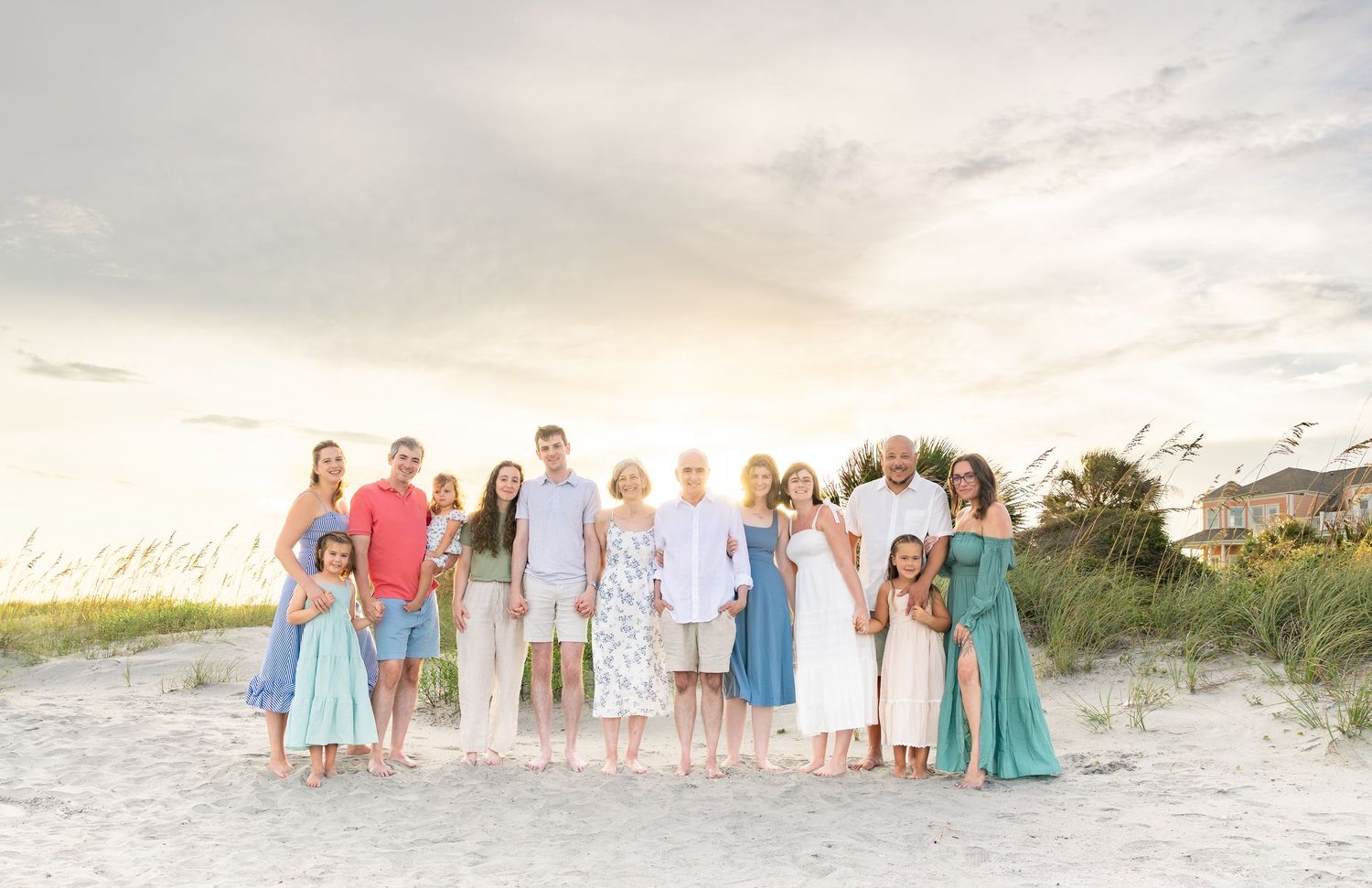 Large family group posing together on a sandy beach at sunset with sea oats in the background.