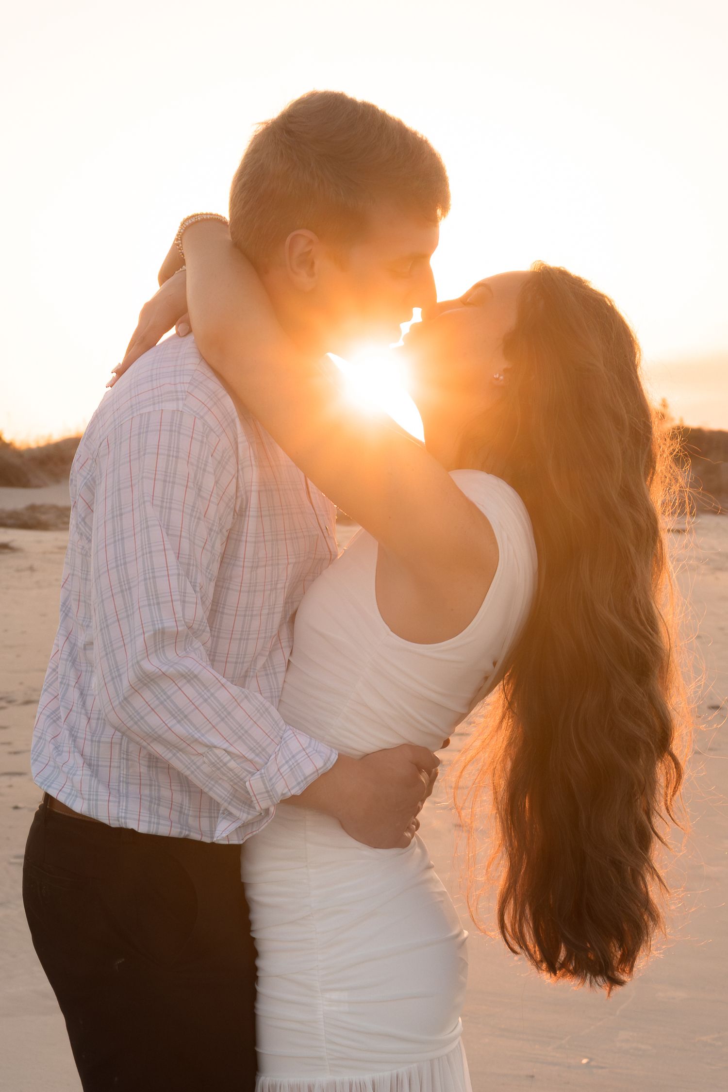 A couple embracing passionately in the sunset on a beach, with the sun's rays shining through them.