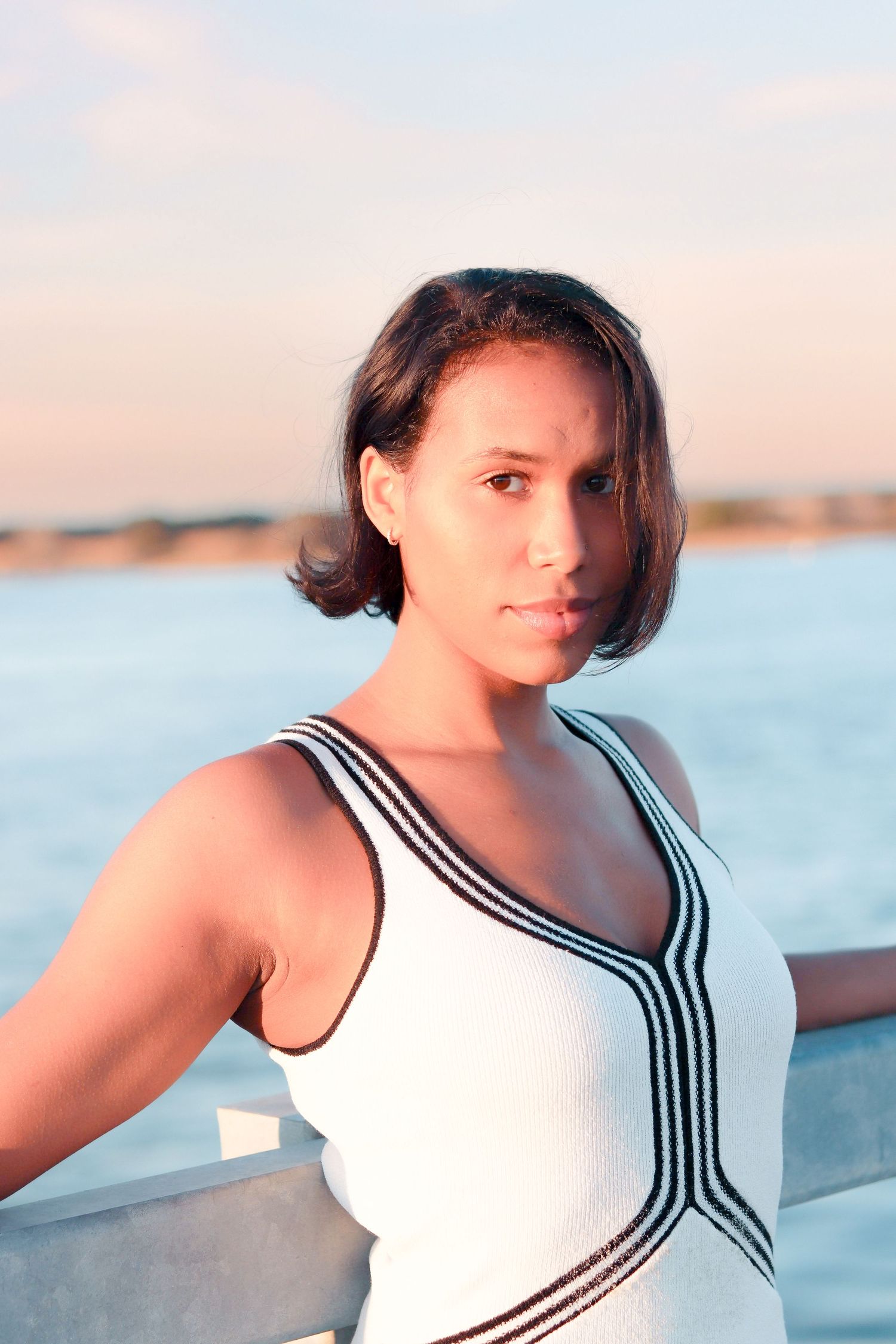 Woman in white and black striped swimsuit posing against ocean backdrop.