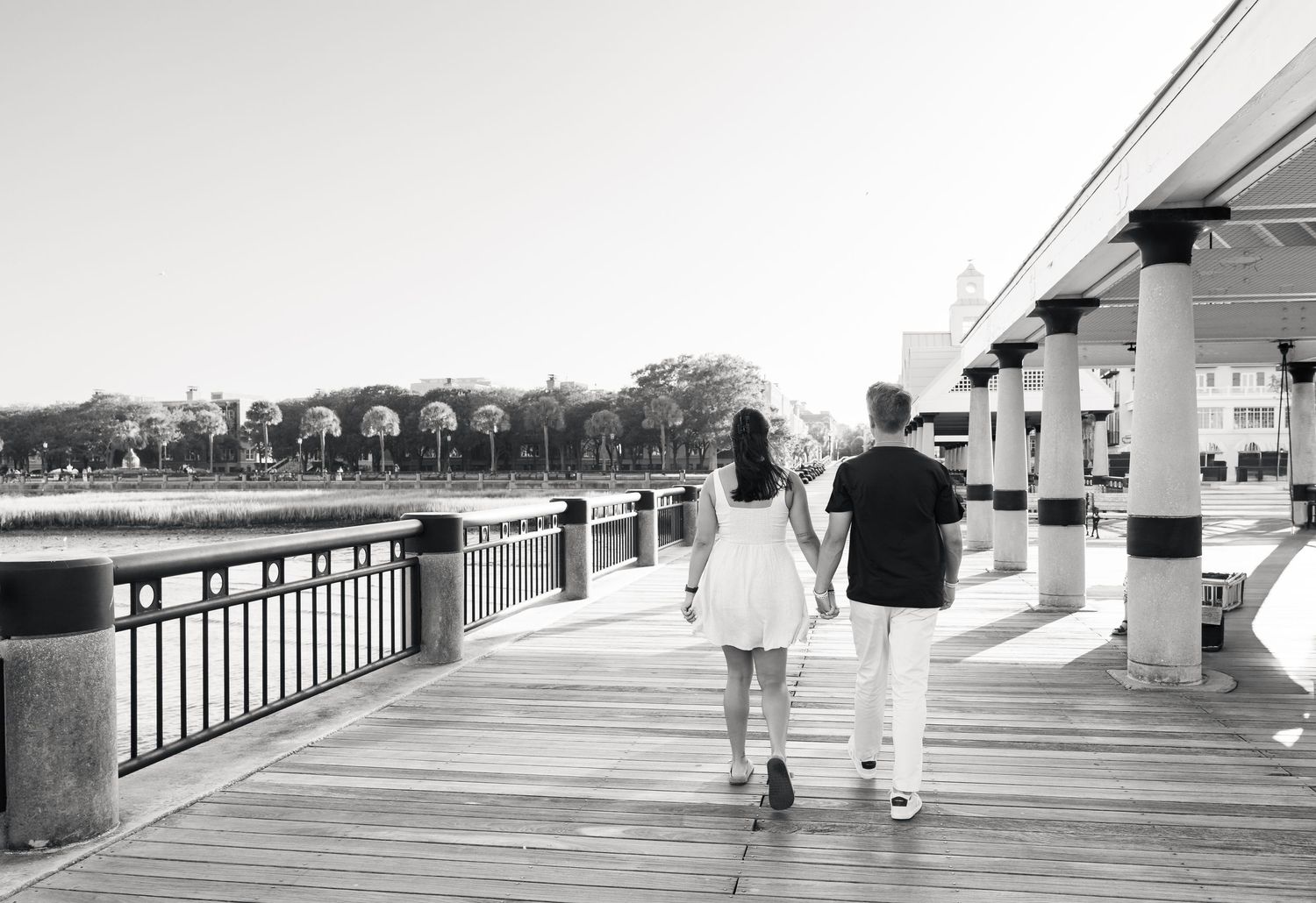 Couple holding hands walking on a waterfront boardwalk in black and white photography.
