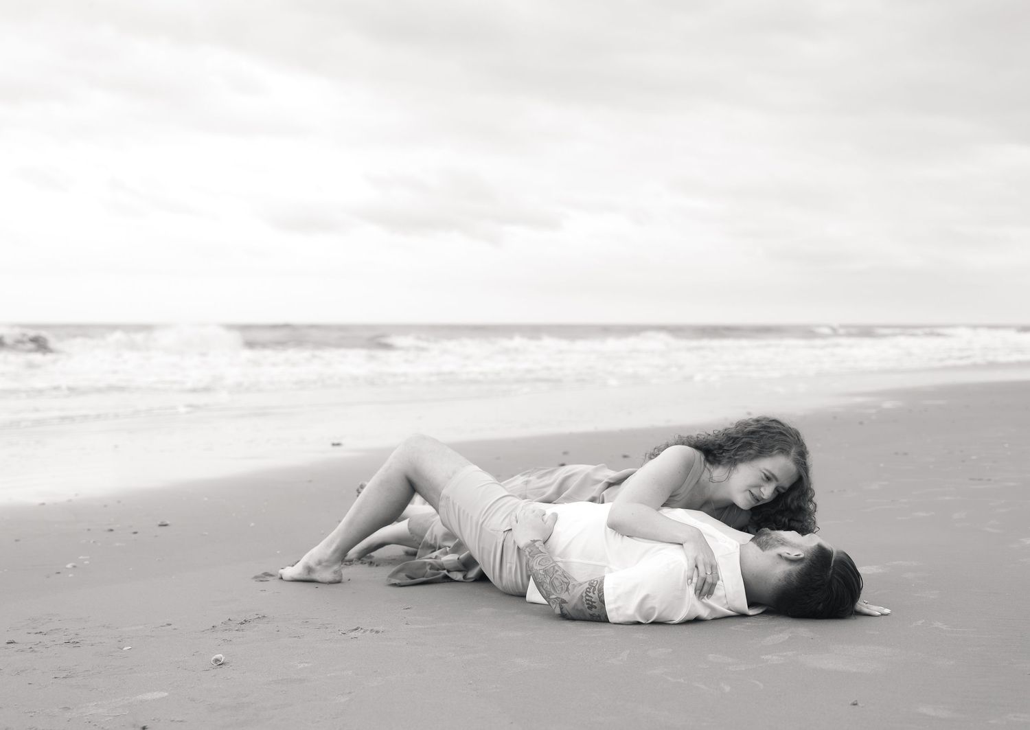 Romantic couple lying together on a sandy beach shore in a tender embrace, black and white photography.