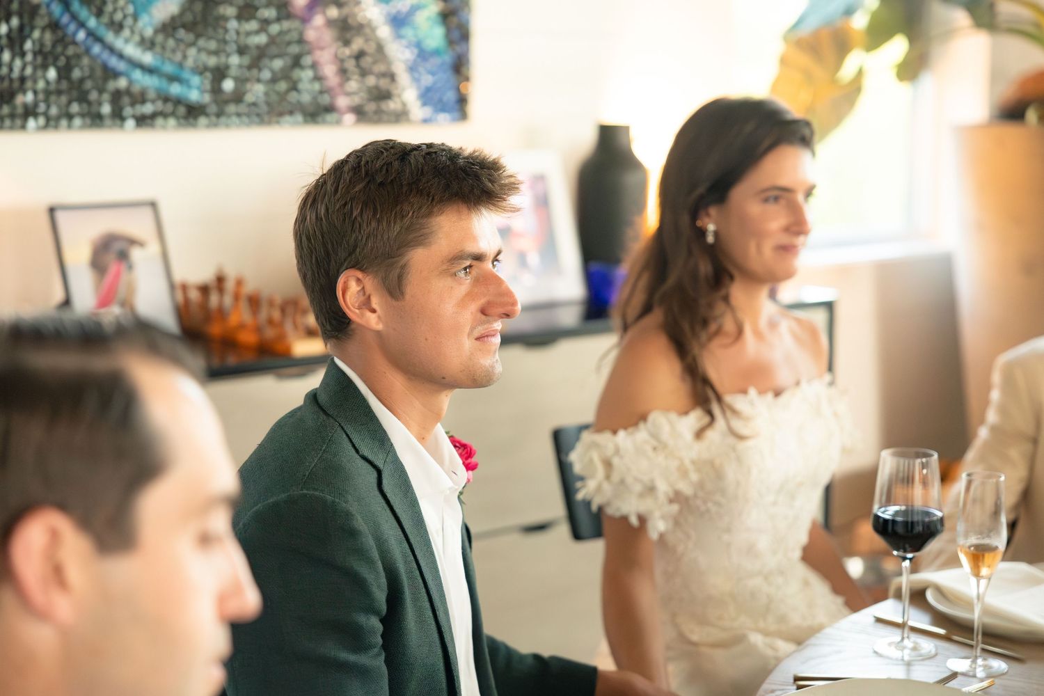 Man in green blazer and woman in white dress seated at an indoor dinner event.