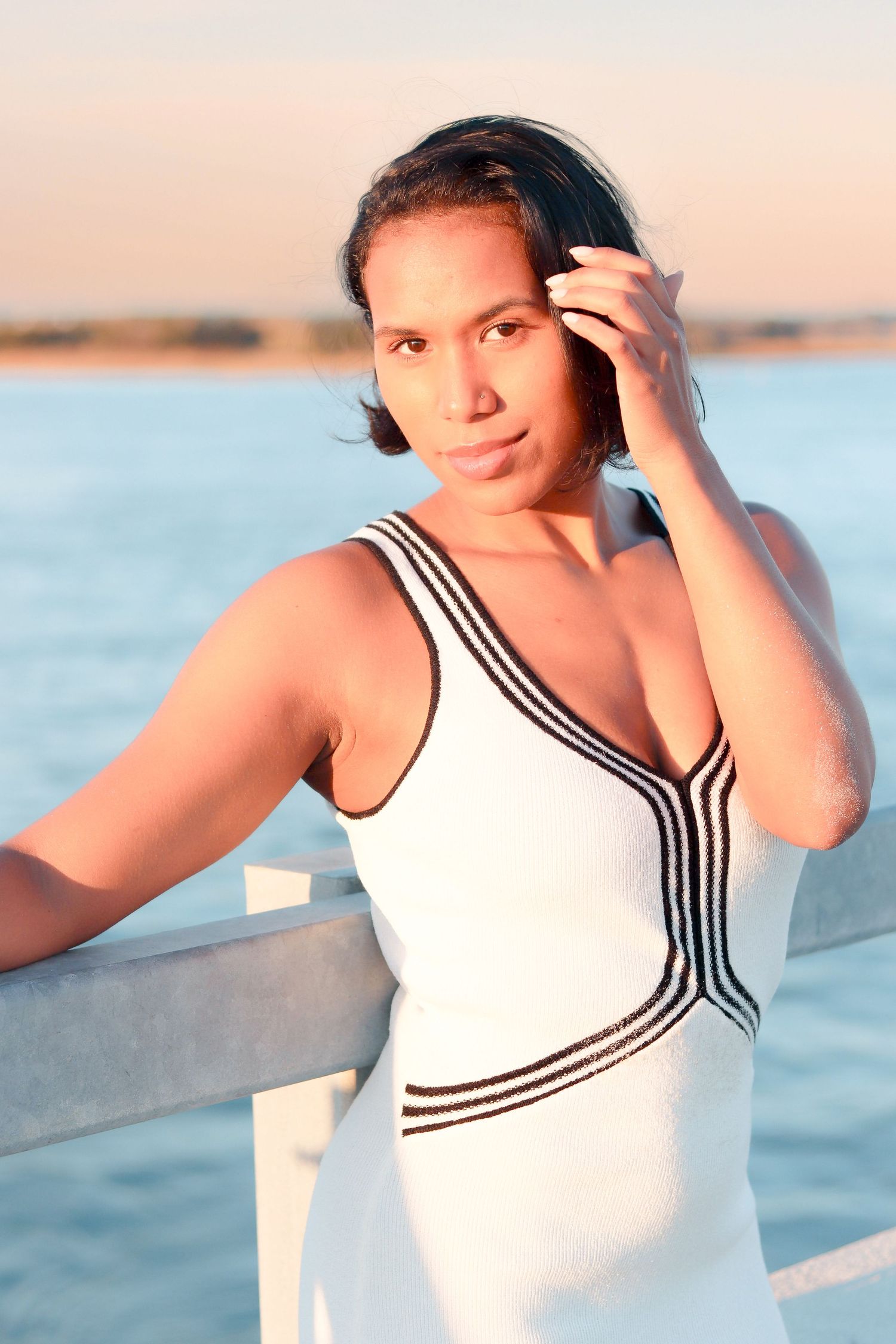 A person in a white sailor-style top poses gracefully against a sunset beach backdrop.