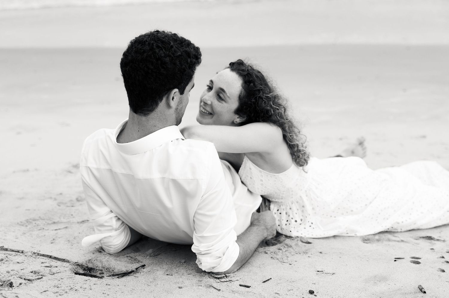 Romantic couple sitting together on a sandy beach in black and white photography.