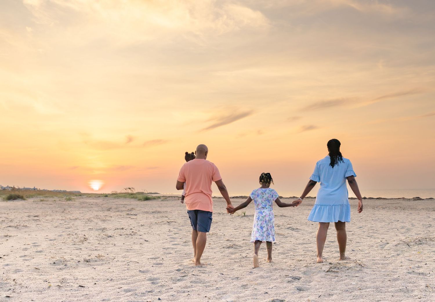 Family holding hands walking toward a beautiful sunset on a sandy beach.