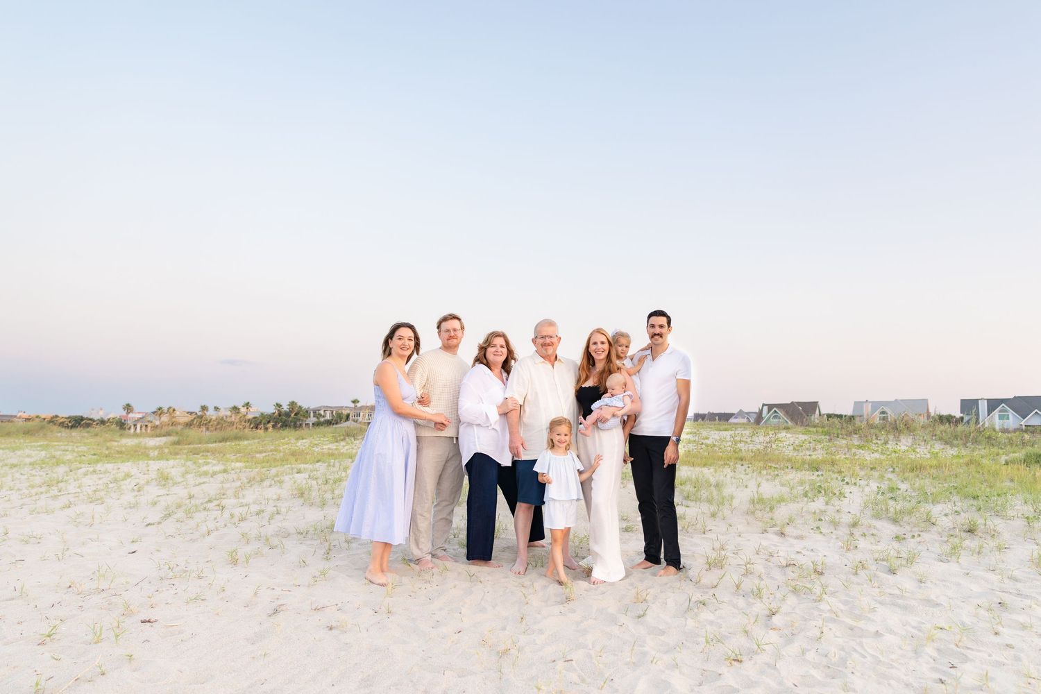 Large family posing together on a sandy beach at sunset, dressed in white and blue outfits.