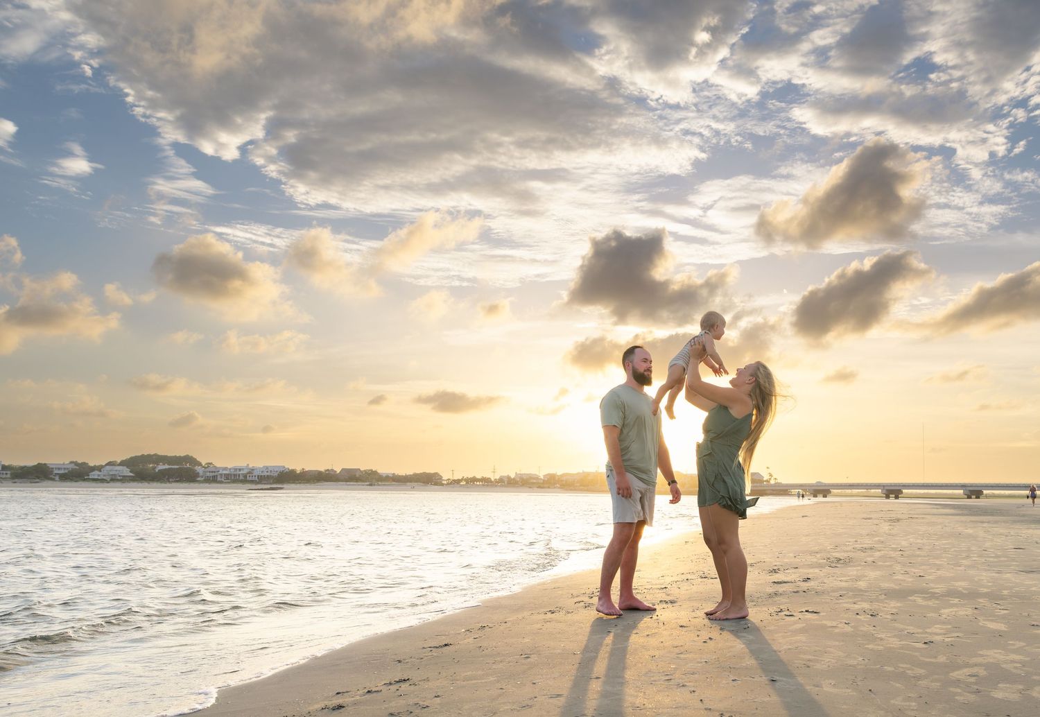 Family enjoying a beautiful sunset on a sandy beach, with parents lifting their baby in the air.