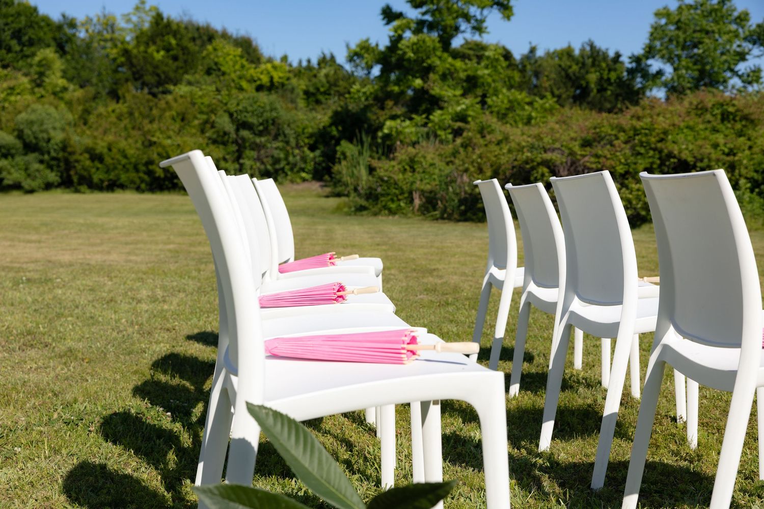 White outdoor chairs arranged on green lawn with pink folded napkins placed on seats.