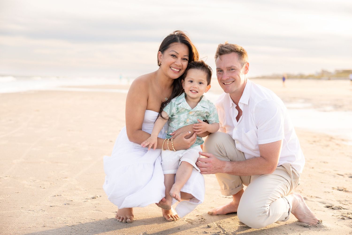 Happy family portrait on beach at sunset, mother and father crouching with smiling baby boy.
