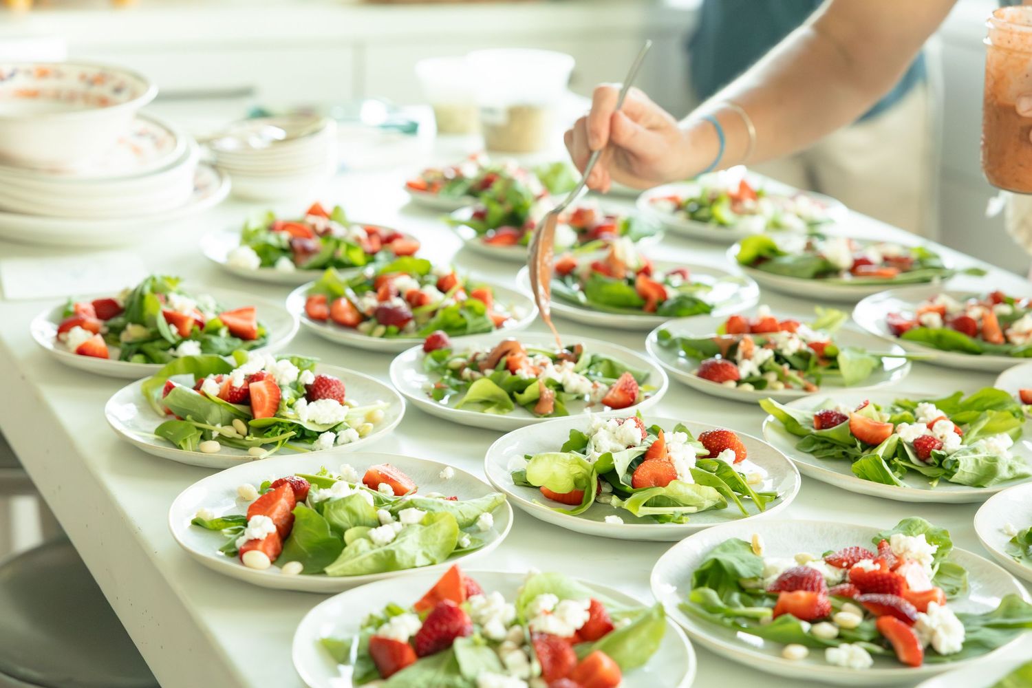 Rows of fresh garden salads with strawberries and feta being plated for wedding reception.