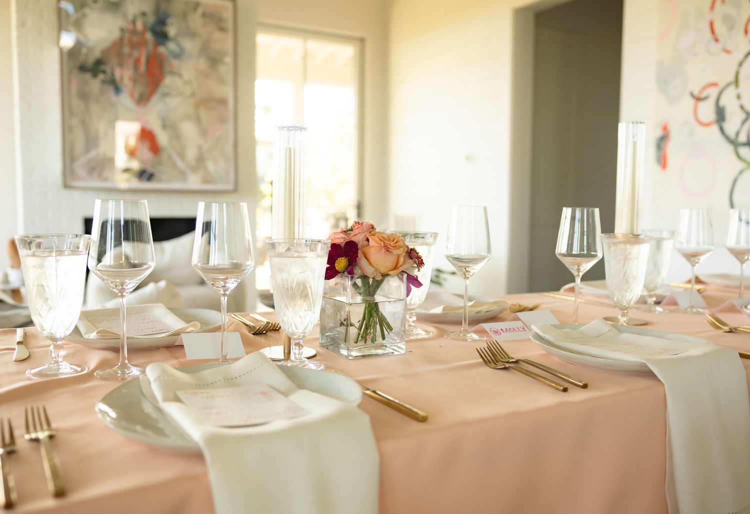 Elegant wedding reception table set with blush linens, crystal glasses, and fresh floral centerpiece.