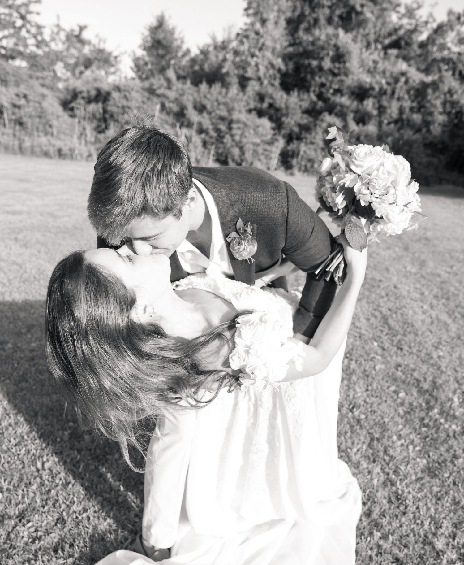 Black and white photo of groom dipping bride for a kiss on grassy lawn.