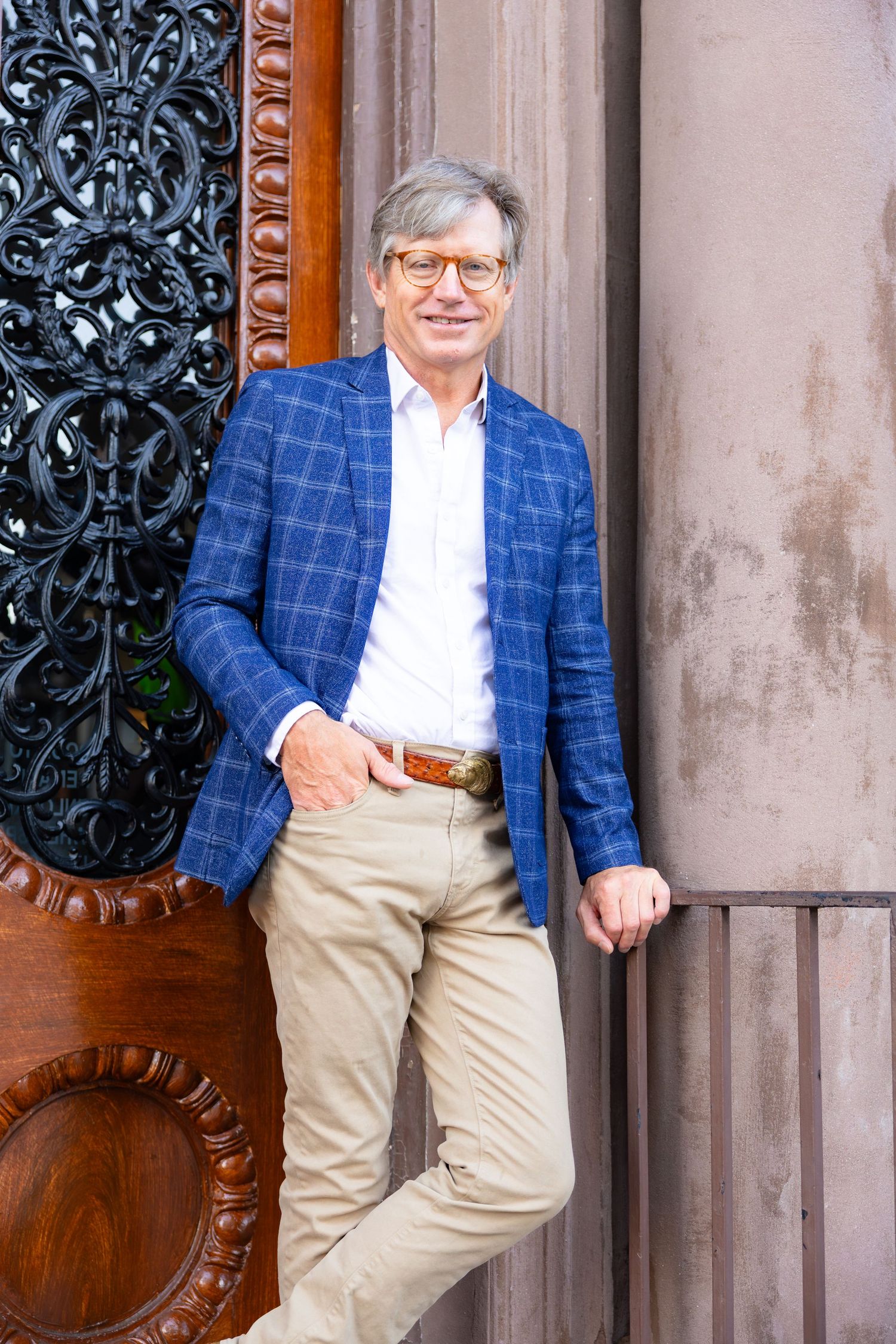 Mature man in blue plaid blazer posing by ornate wooden door outdoors.