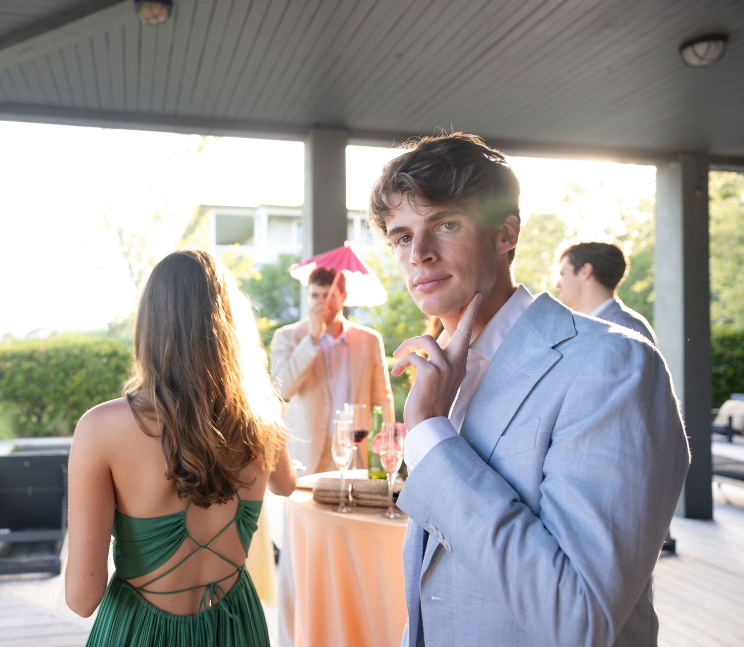 Young man in light blue suit adjusts collar at outdoor wedding cocktail hour reception.