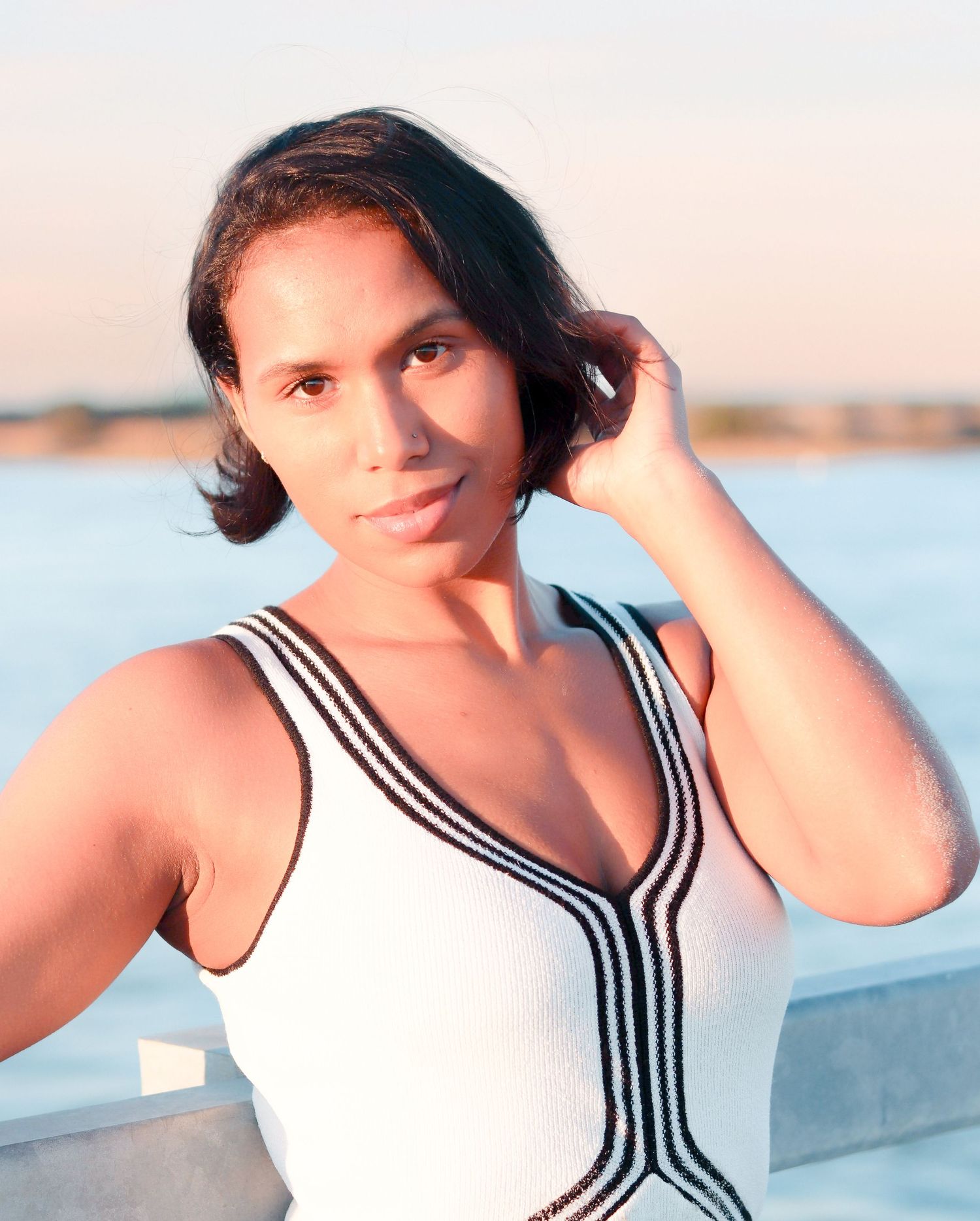 A series of photos showing a person in a white swimsuit with black stripes posing by the water at sunset.